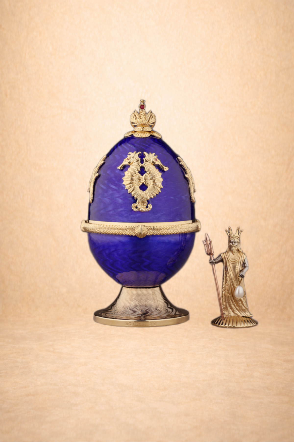 A decorative blue and gold goblet with a crest featuring a double-headed eagle, accompanied by a small figurine of a king wearing a crown and robe, holding a scepter.