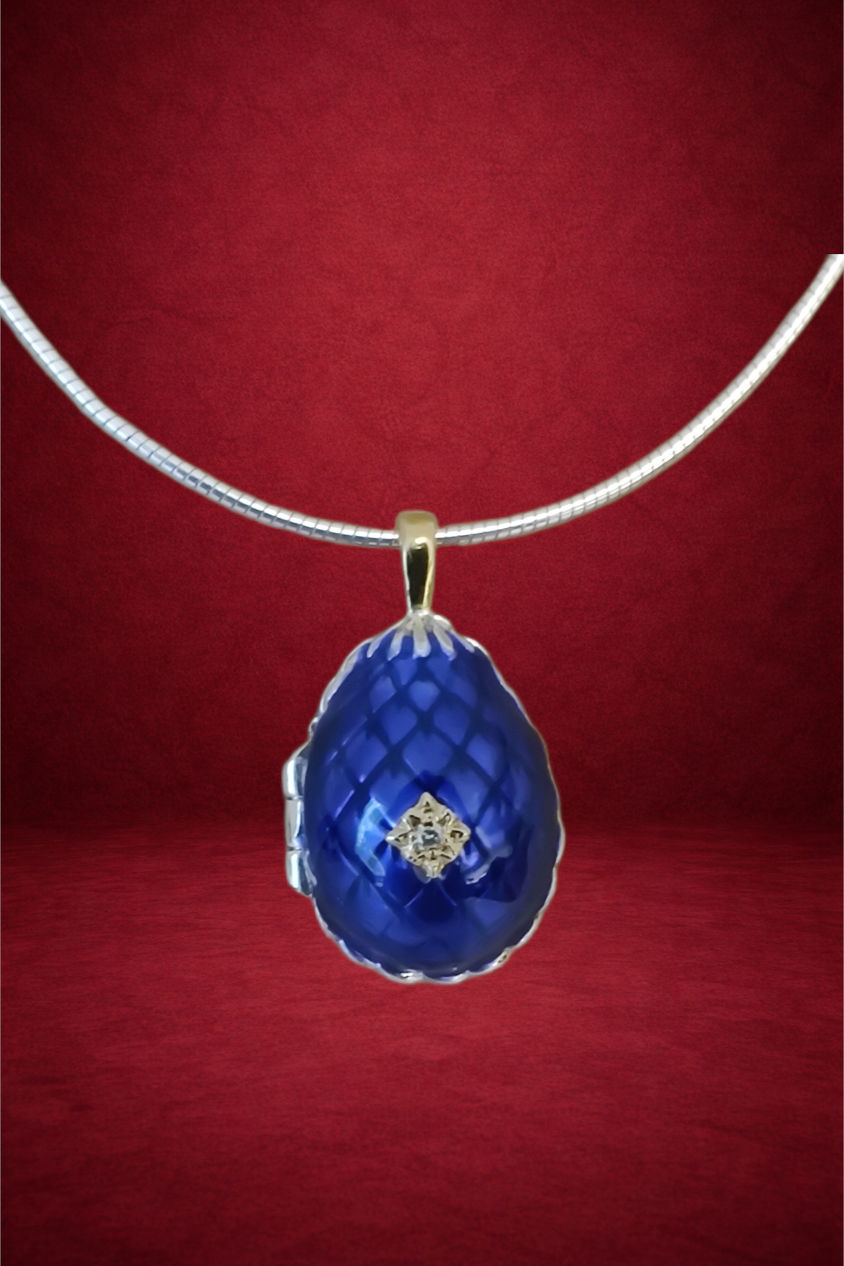 A silver necklace with a blue teardrop-shaped pendant featuring a small diamond in the center, hanging against a red background.