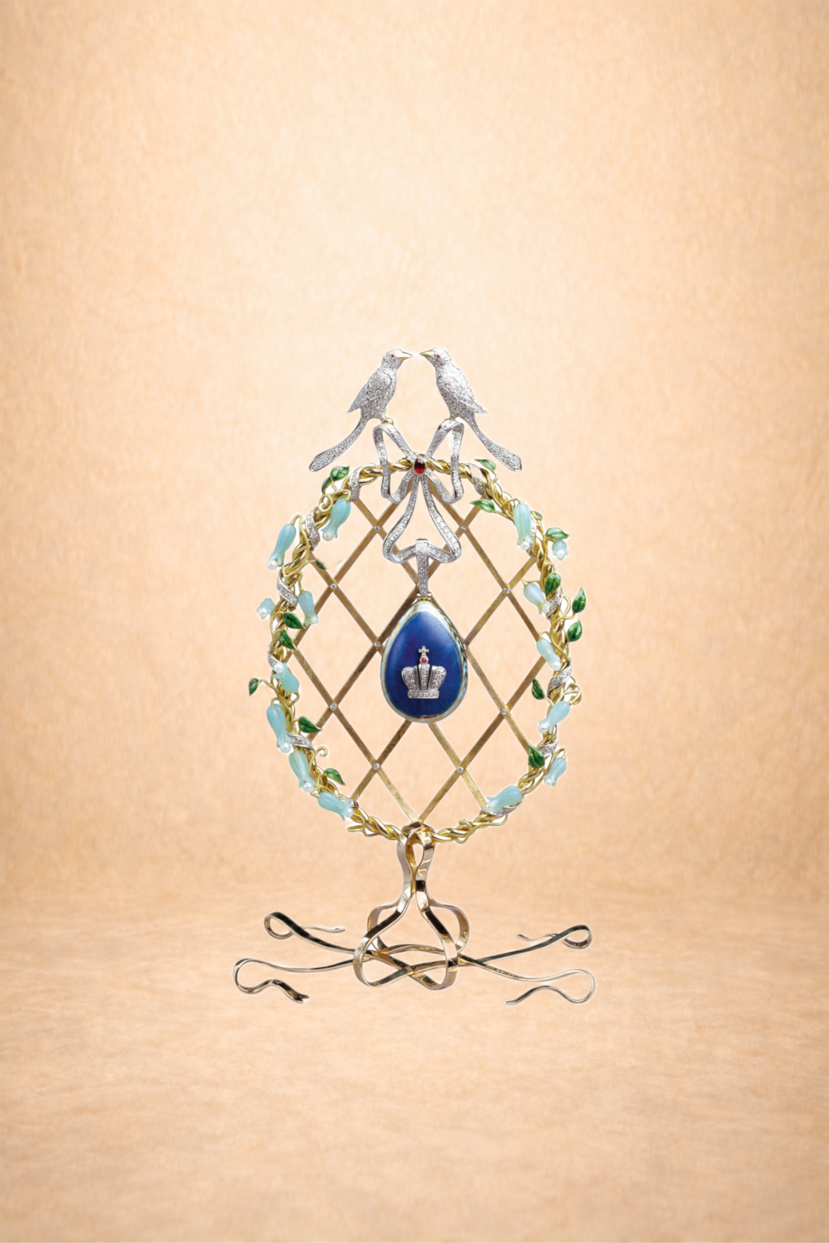A decorative jewelry piece with two birds on top, a royal crown on a blue background, and a gold lattice frame adorned with light blue and green accents.