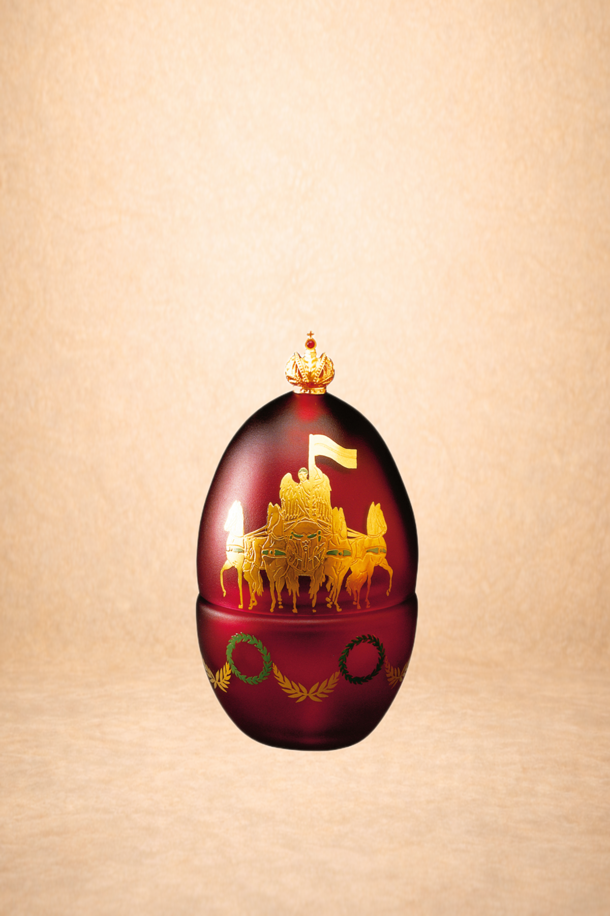 A decorative red egg with gold and green designs, featuring a royal crest with a chariot and horses, topped with a small crown.
