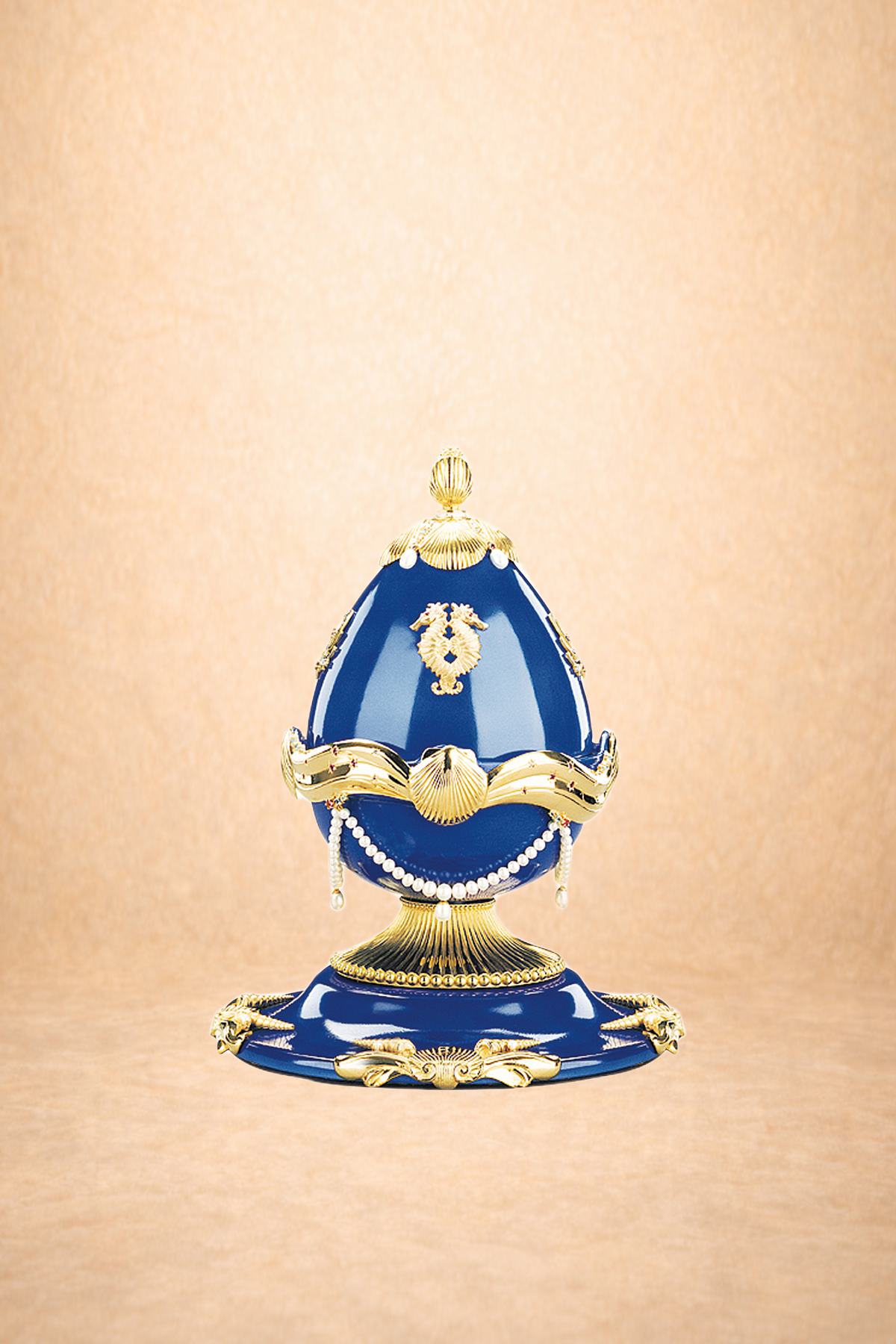 Decorative porcelain egg with royal blue and gold accents, adorned with pearls, placed on a matching blue and gold stand.