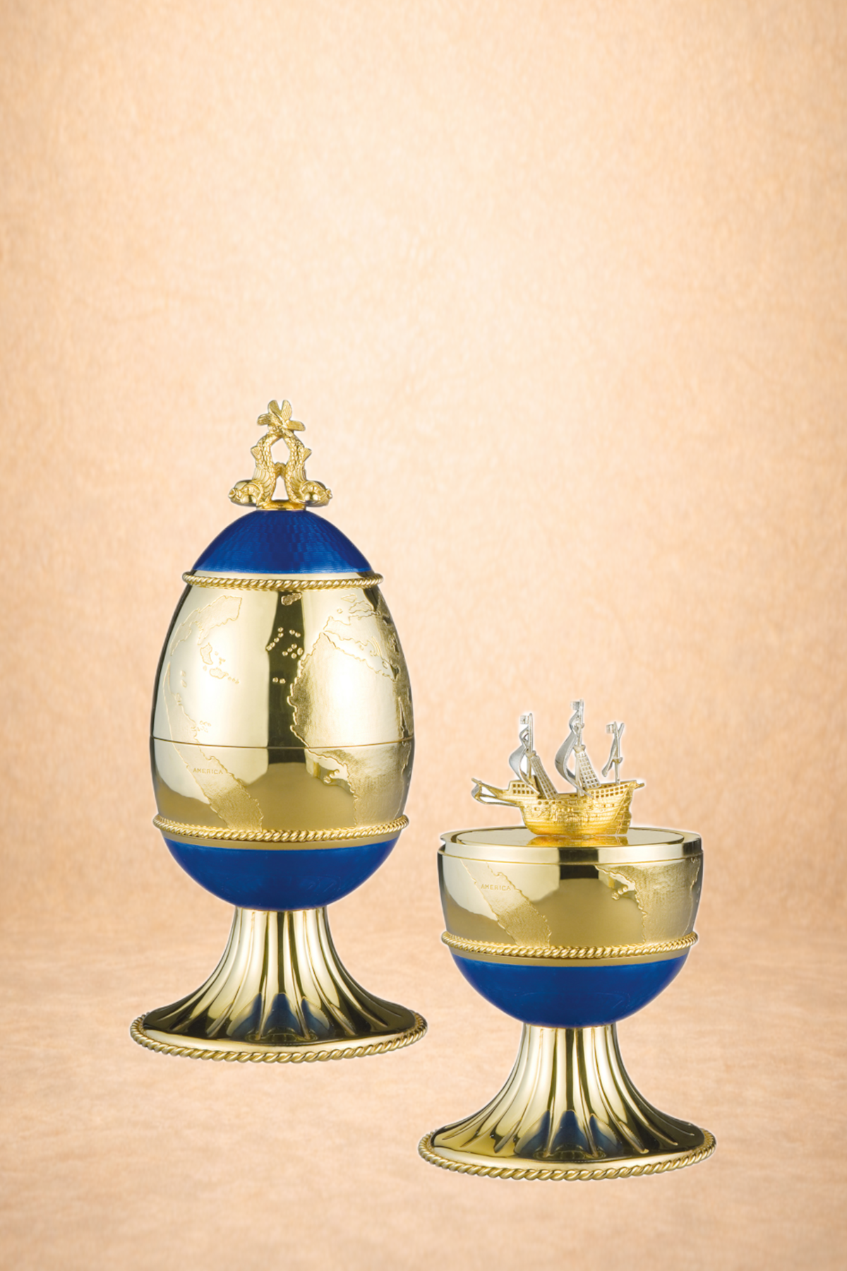Two decorative globes with gold and blue accents, mounted on gold bases, one topped with a gold monument of two lions and the other with a gold miniature ship.