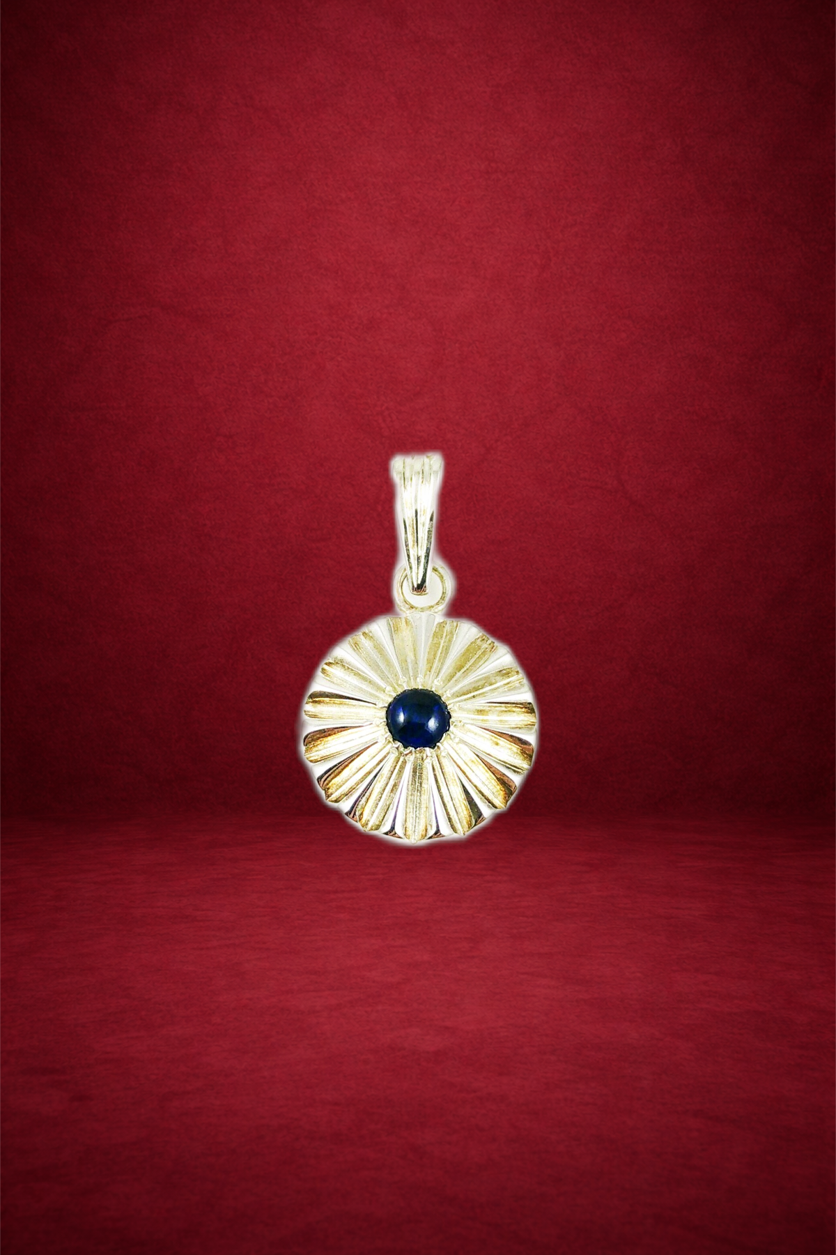 Gold pendant with sunray design and a dark blue center stone on a red background.