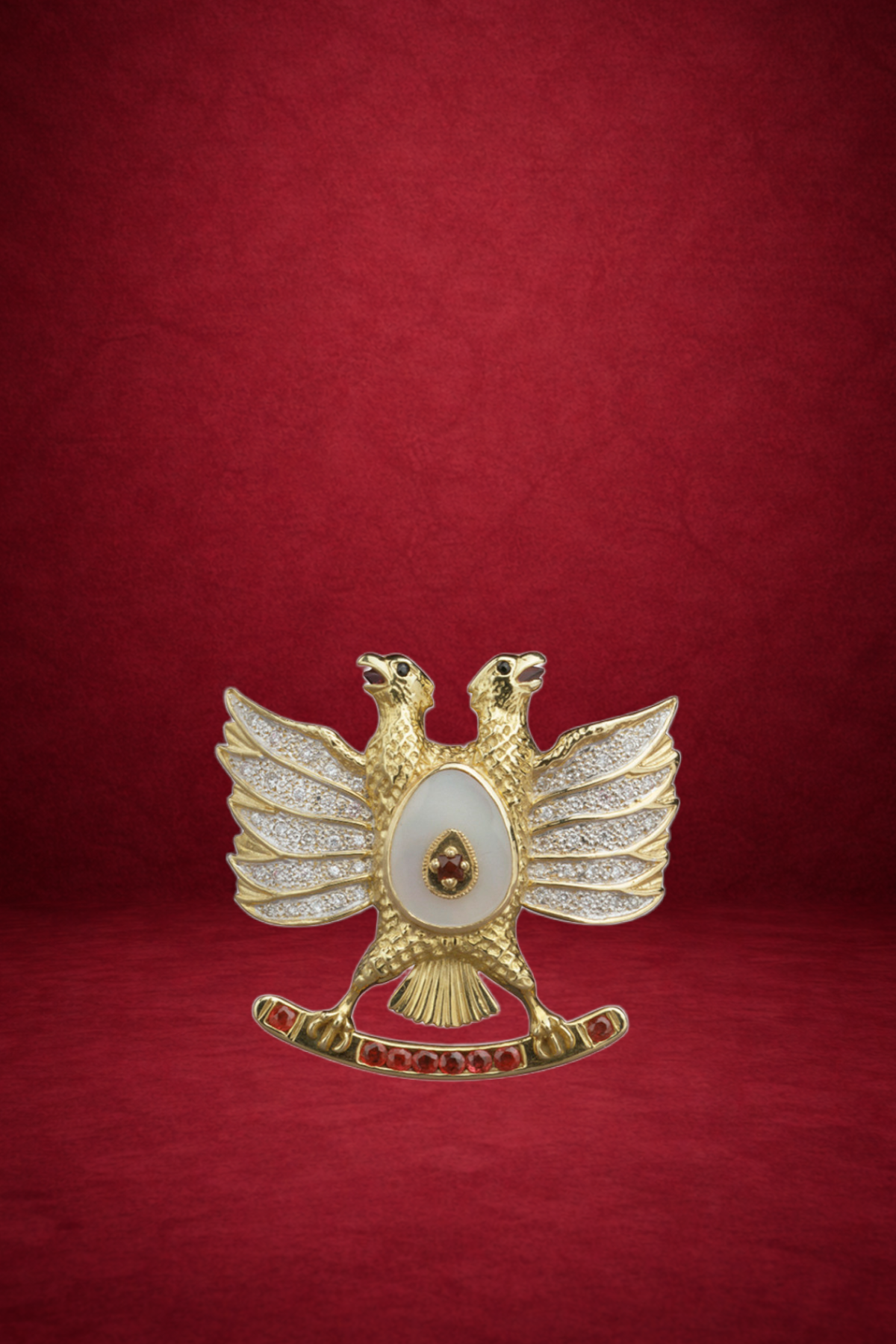 Gold ornament in the shape of a bird, decorated with diamonds and red gemstones, placed on a red background.