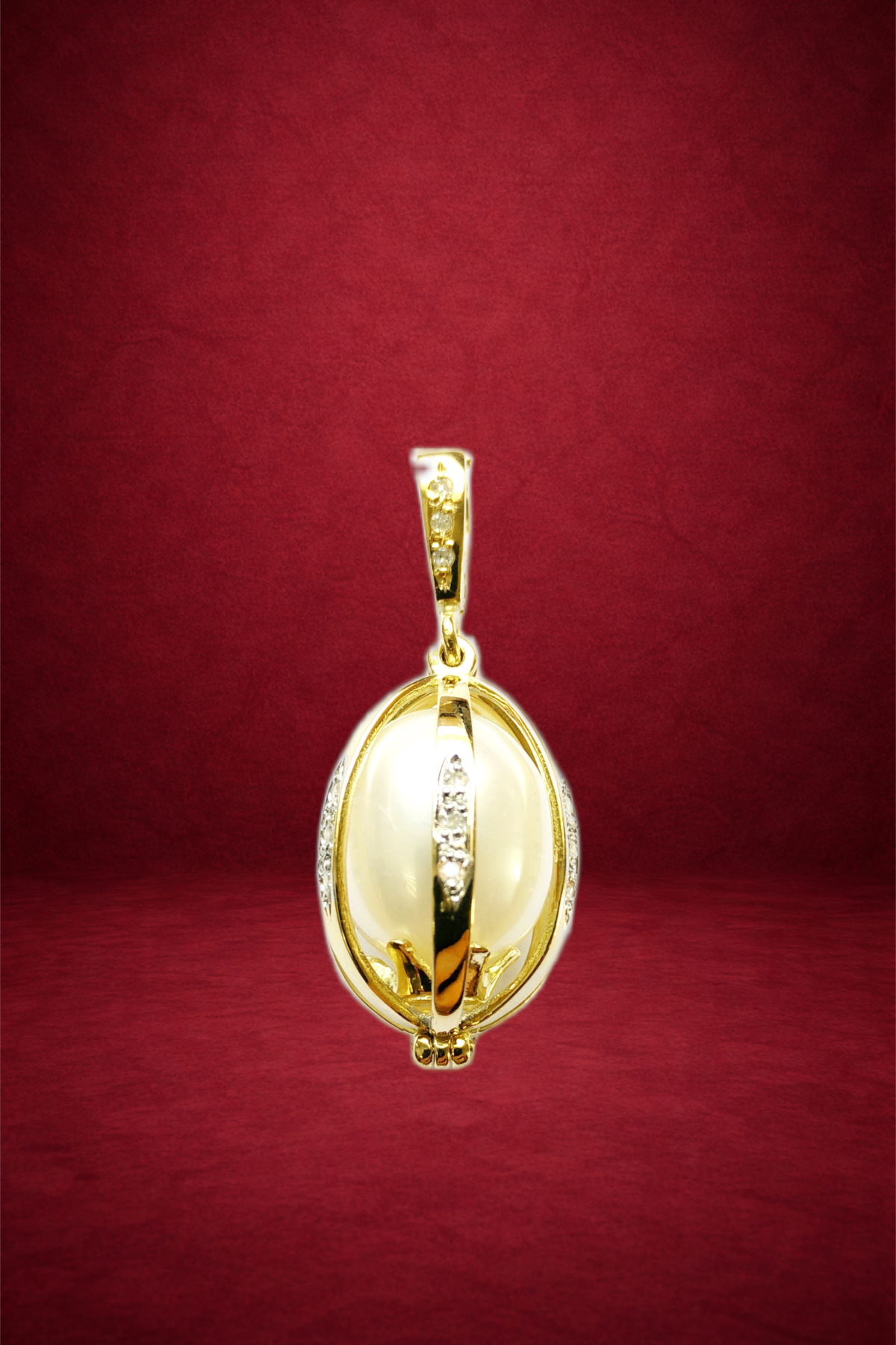 Gold pendant with a large pearl and embedded diamonds on a red background.
