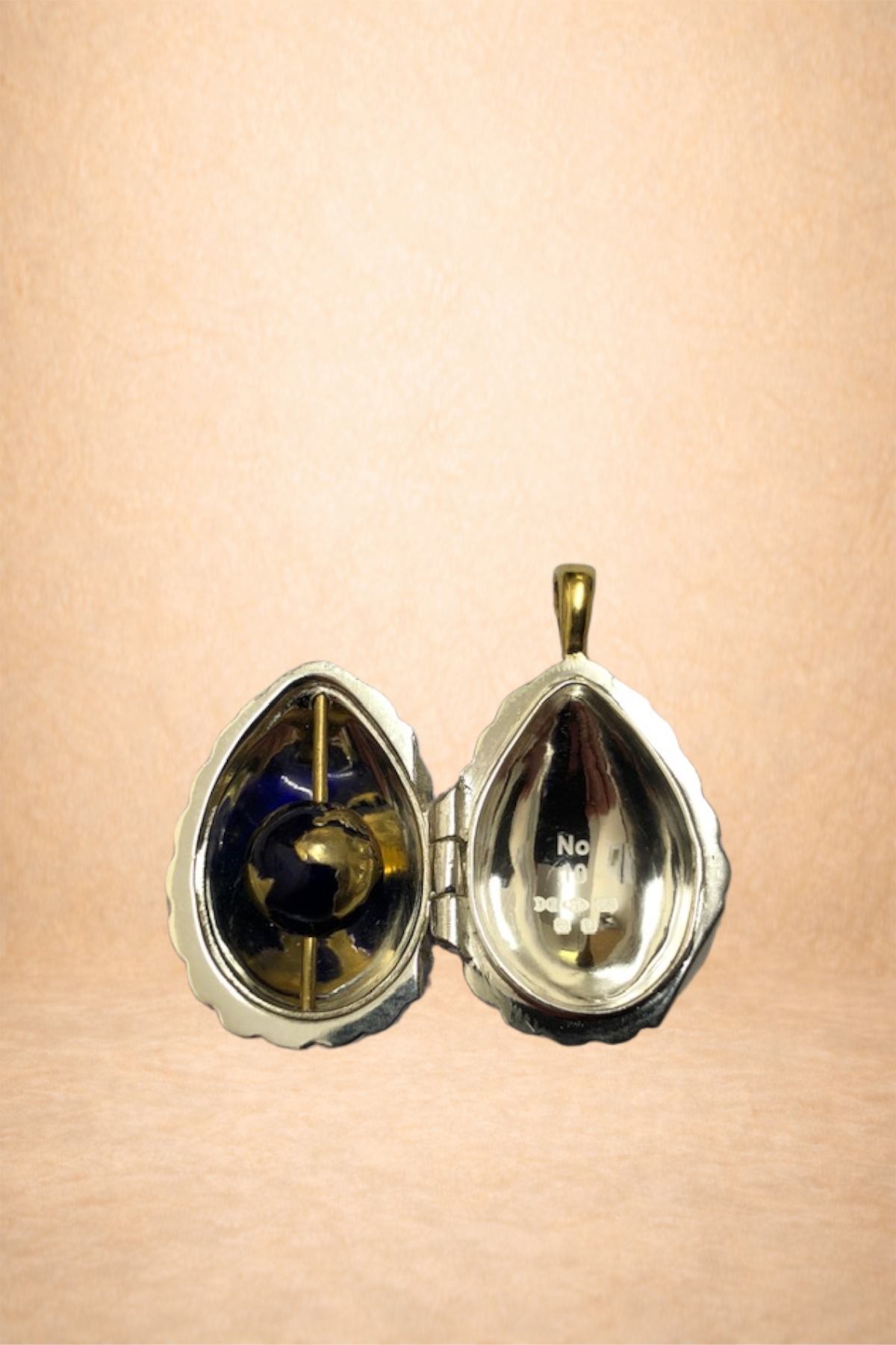 A metallic silver and gold open heart-shaped jewelry box with a black and gold spherical object inside on a light background.