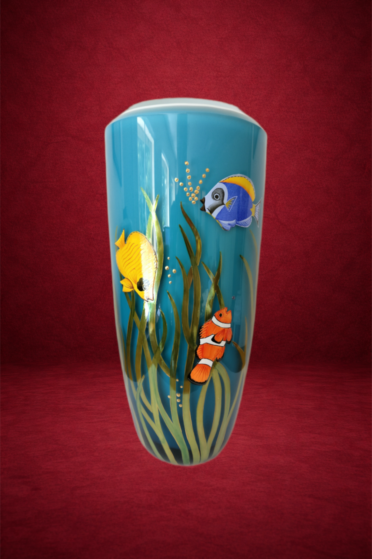 A tall, cylindrical, glass vase with an underwater scene of colorful tropical fish and seaweed painted on it, set against a red background.