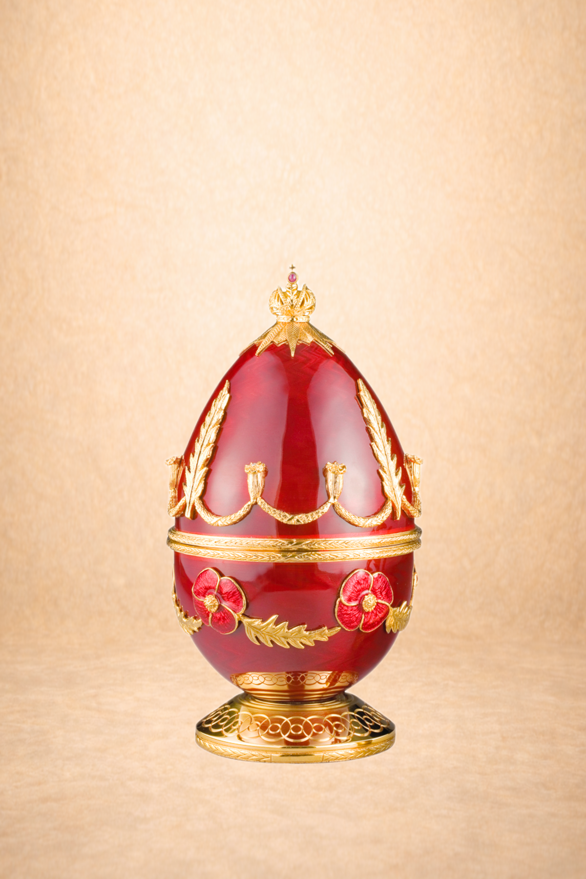 Decorative red and gold egg-shaped ornament with floral and crown motifs, on a gold stand.