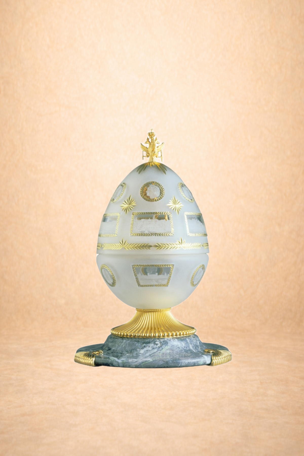 Decorative Egg-shaped ornament with gold accents, on a gold and marble base, with a gold crown on top, set against a peach-colored background.