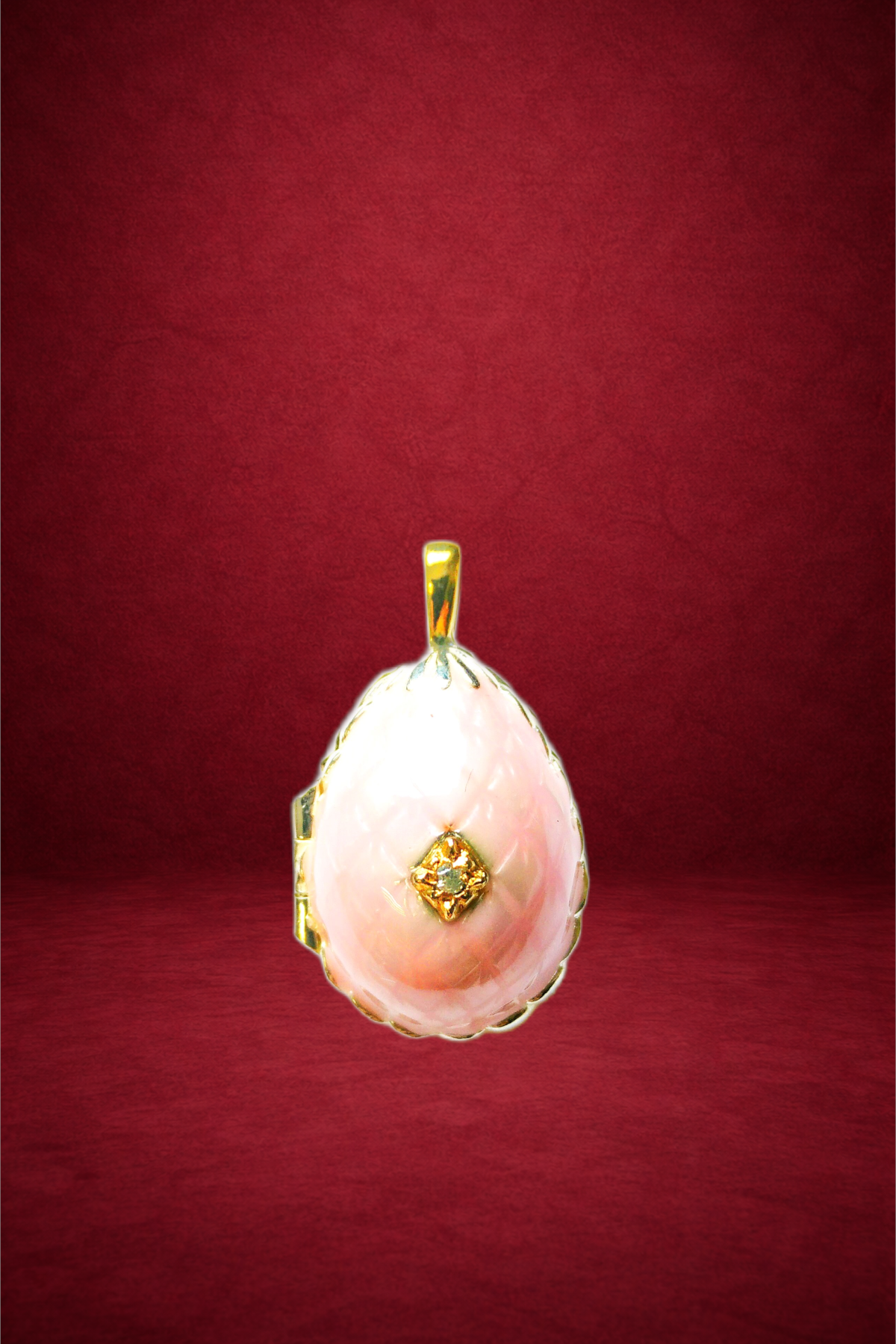 A gold pendant with a large pink pearl and small diamonds on a red background.