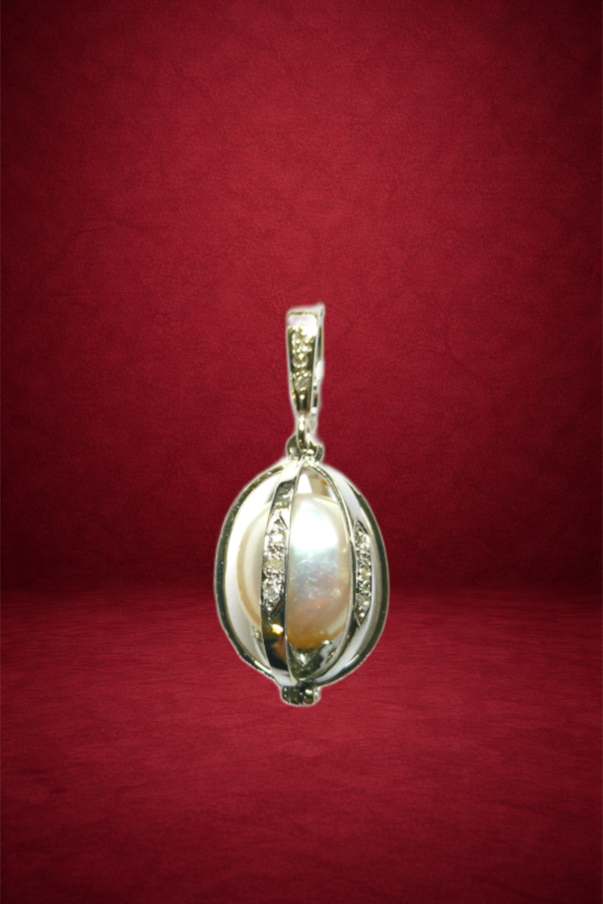A silver pendant with a central pearl and diamond accents, hanging against a red background.