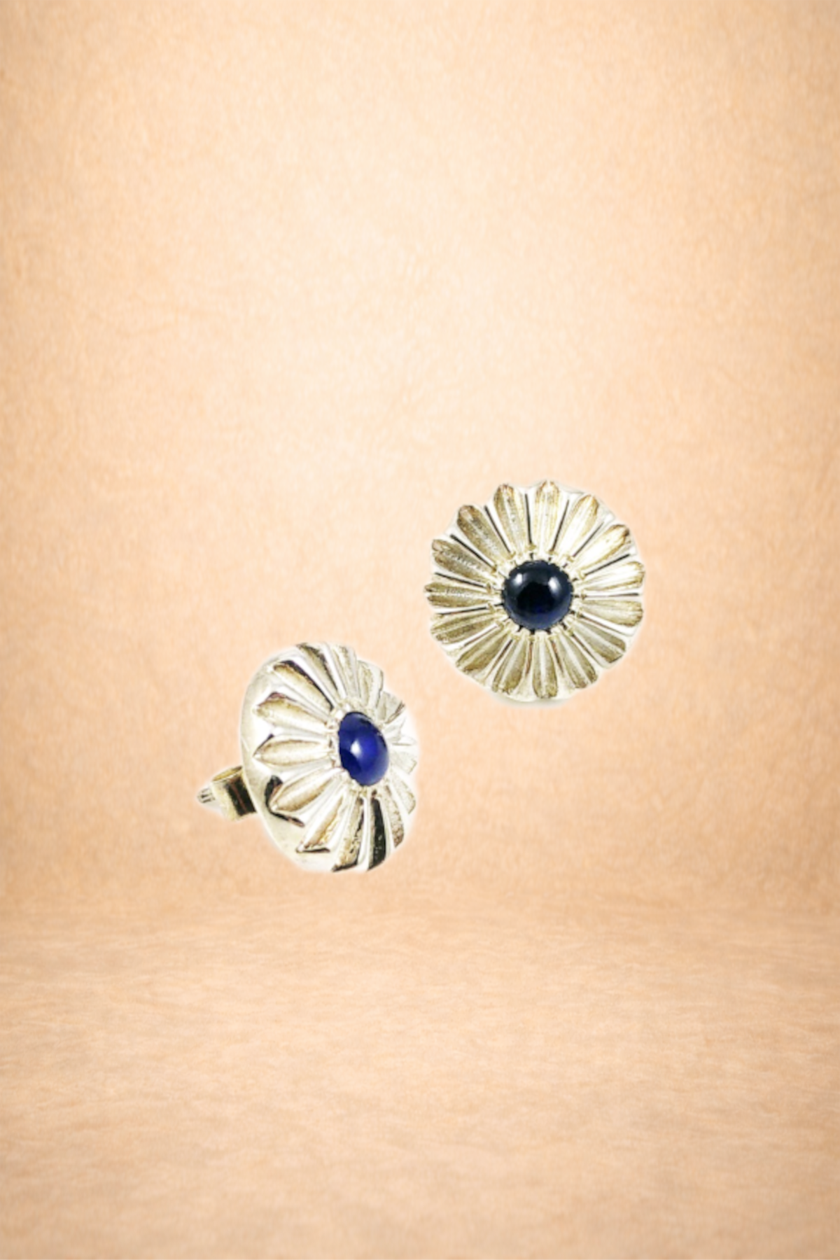 Silver floral-shaped earrings with a dark blue gemstone center, suspended against a beige background.