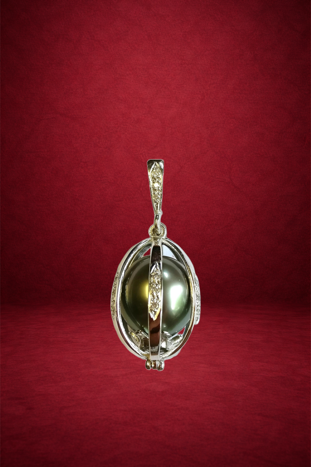 A pendant with a greenish-black pearl encased in an ornate silver setting, hanging from a small loop with intricate details, against a red background.