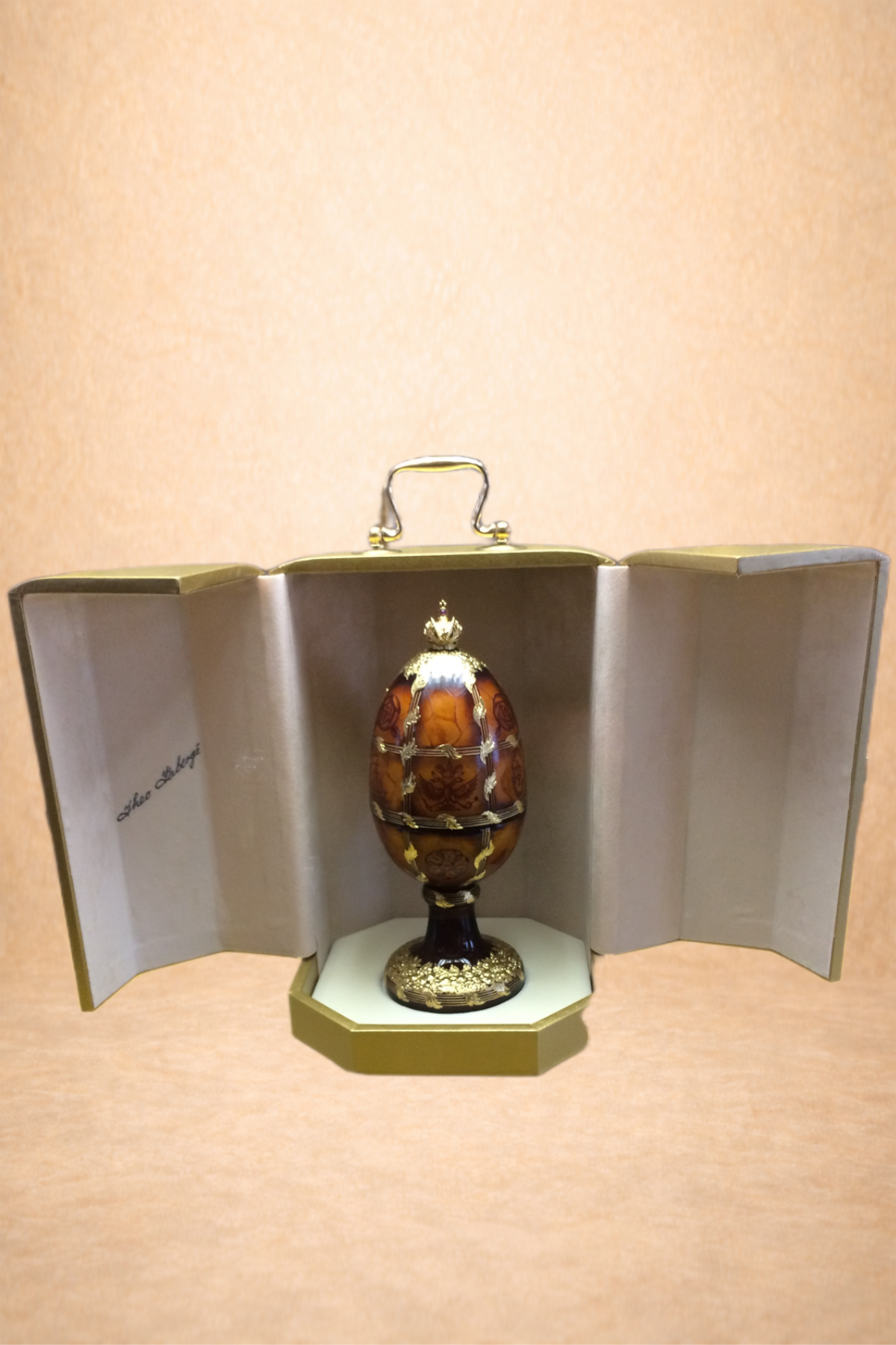 A decorative egg-shaped object inside an open box with gold exterior, shown on a light-colored surface.