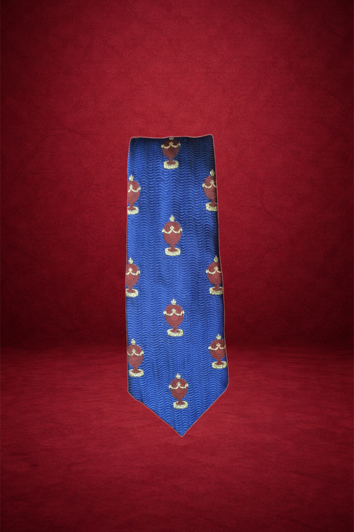 A blue necktie with a repeating pattern of red urns with gold accents, set against a red background.