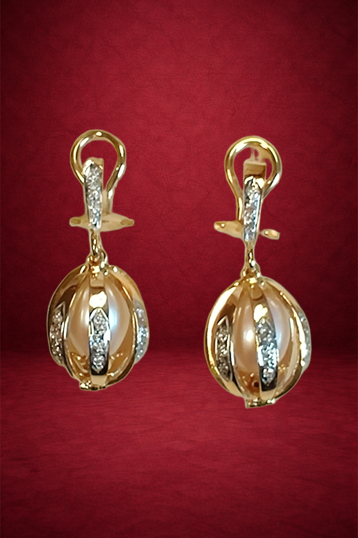 Gold earrings with a spherical design, adorned with clear gemstones, set against a red background.