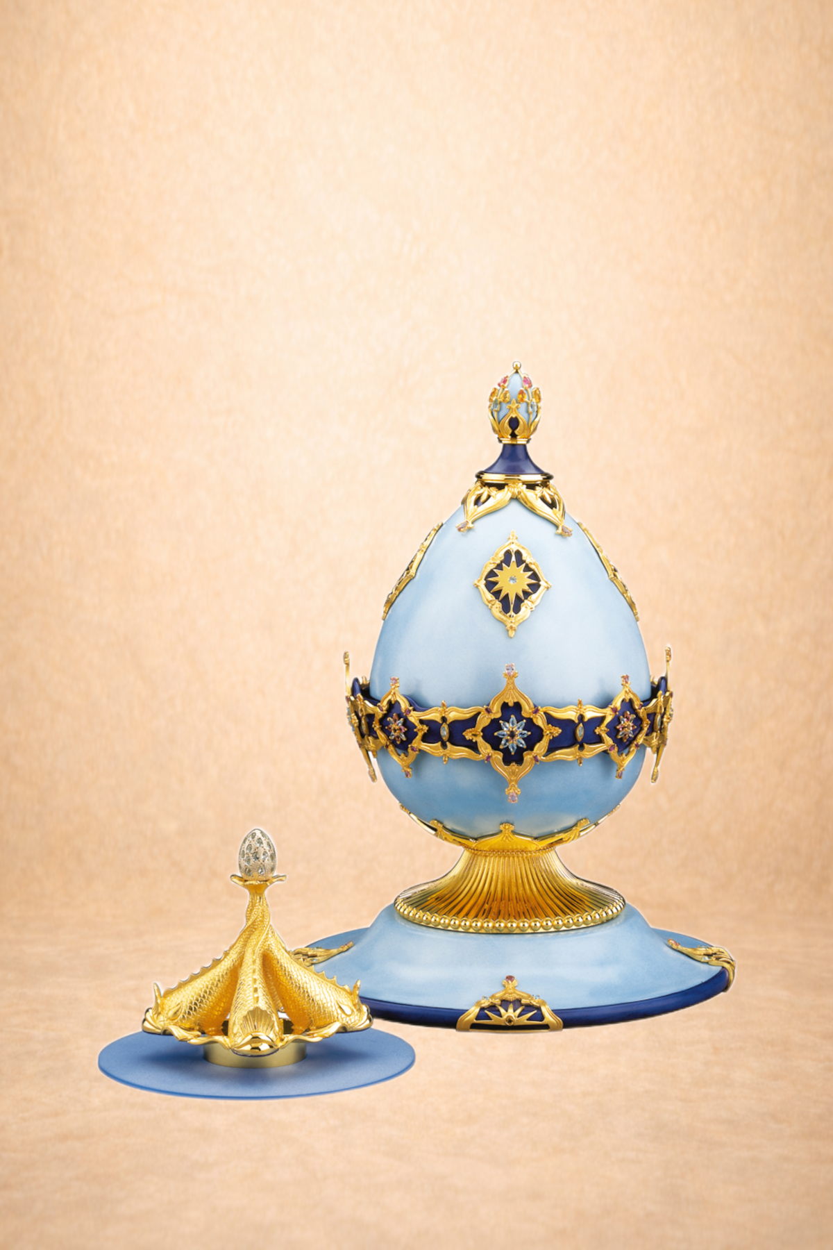 A decorative crown with gold, blue, and white elements, set on a blue base with gold accents and motifs, against a peach-colored background.