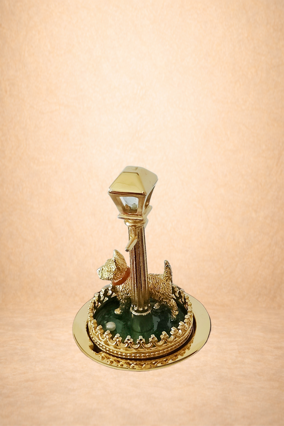 A decorative gold-colored tabletop fountain with a dog figure and a lamppost on a round base with a green interior.