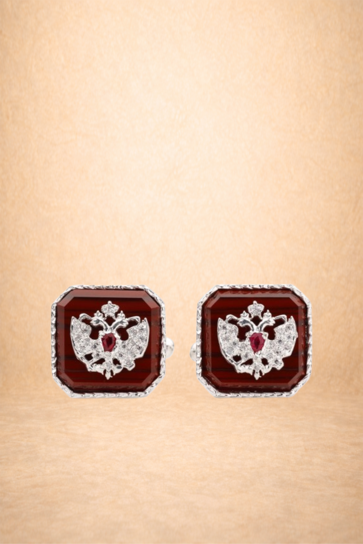 Pair of square-shaped earrings with a crown and double-headed eagle design, featuring white and red gemstones on a gold background.