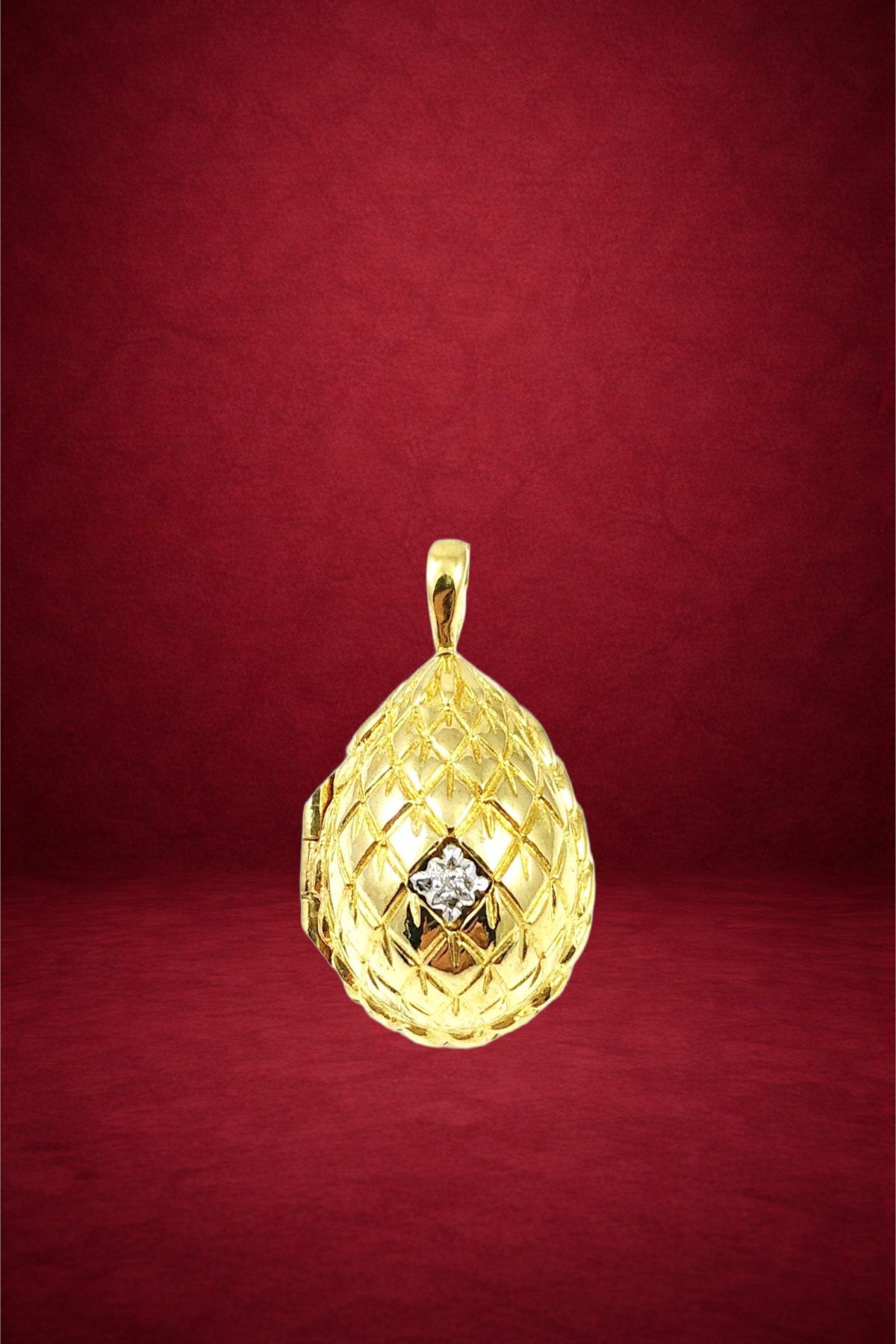 Gold pendant with a lattice pattern and a central diamond, hanging against a red background.