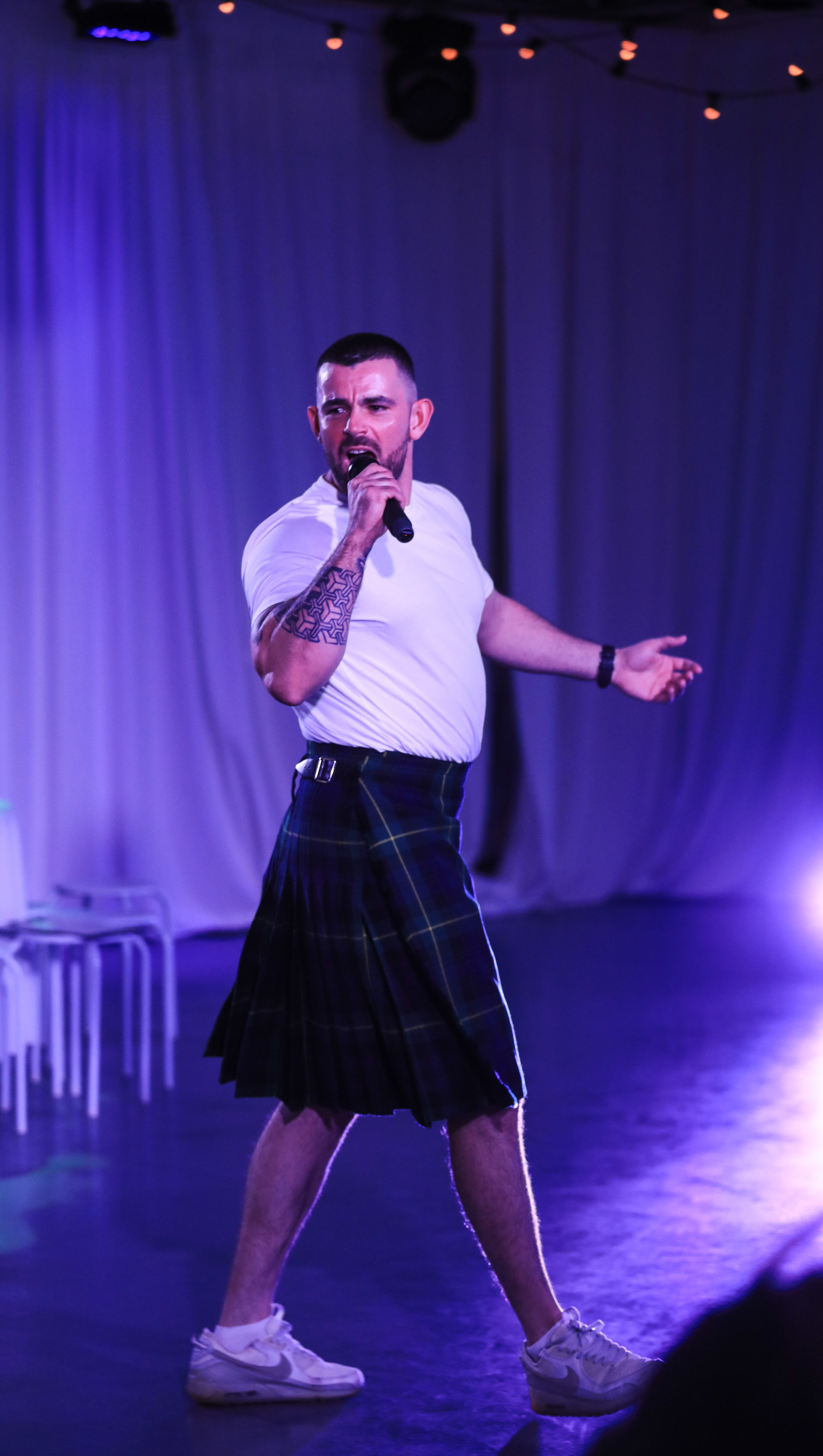 male performer in white t'shirt and kilt with microphone