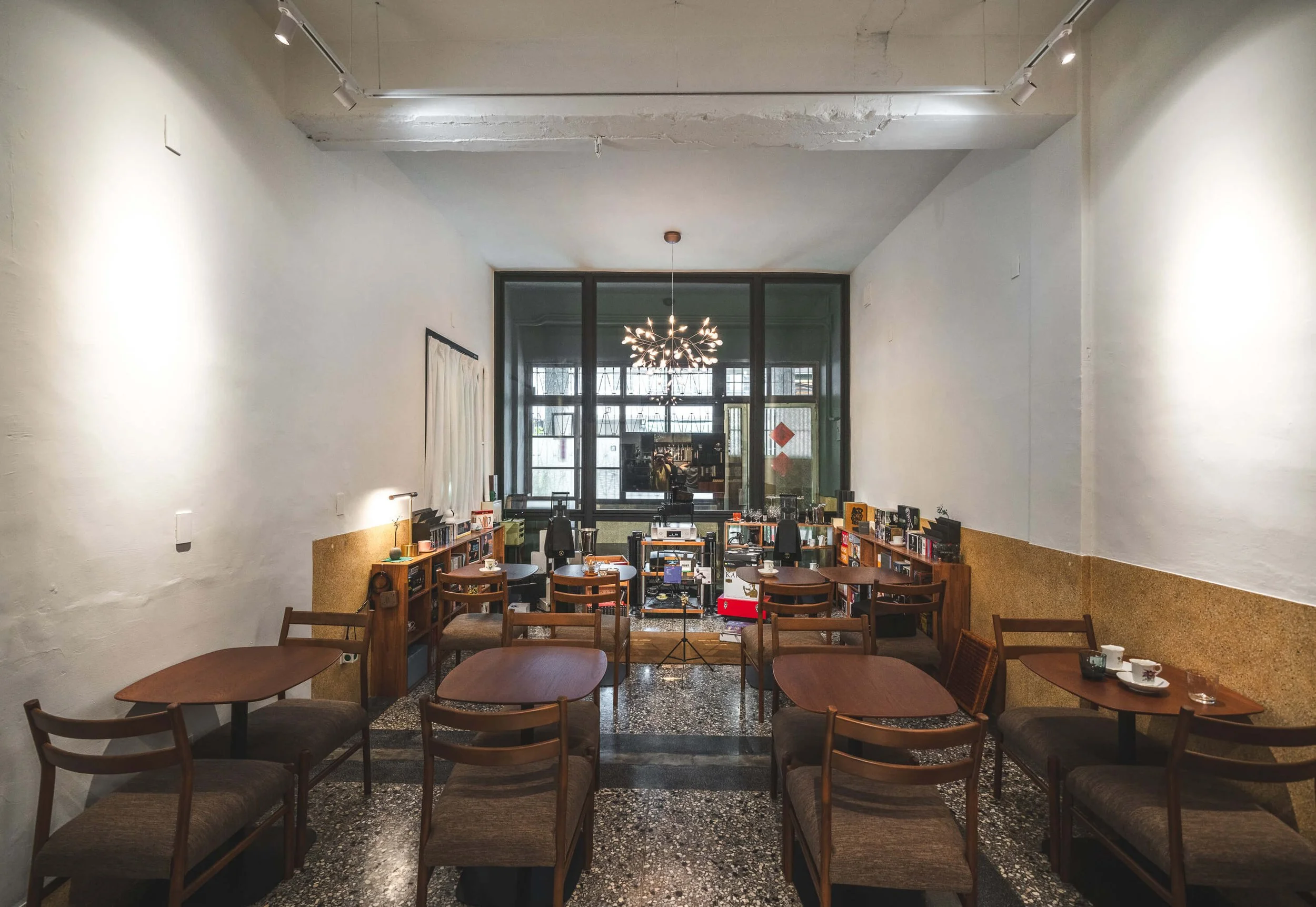 台中 Until 室內設計 Feng Cafe 奉咖啡挑高座位區，白色高牆與深色花窗，水晶吊燈下為木色桌椅、磨石子地坪與黃褐色紋理牆面