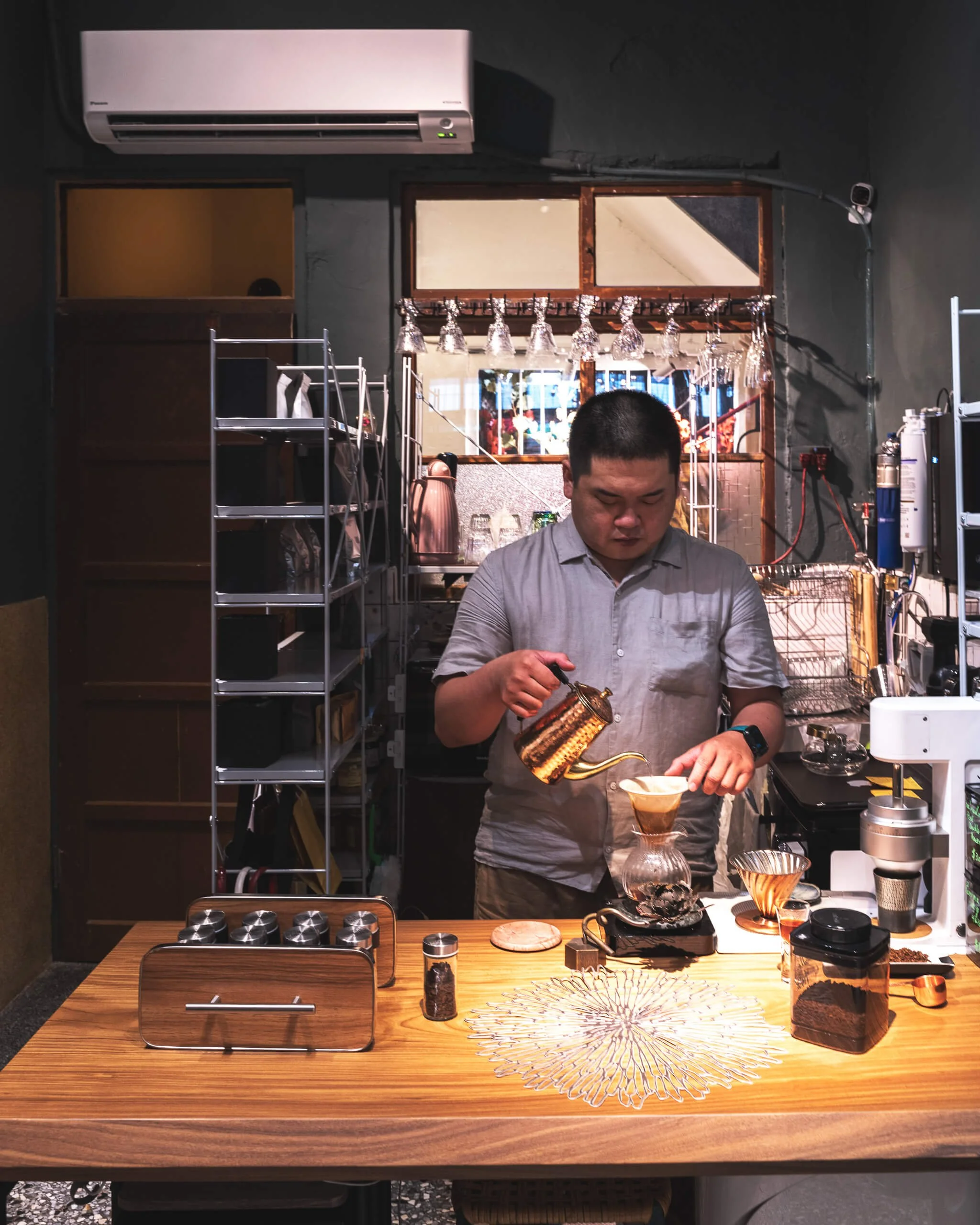台中 Until 室內設計 Feng Cafe 奉咖啡吧檯，咖啡師在實木吧檯後方手沖咖啡，後方為杯具展示架與金屬層架