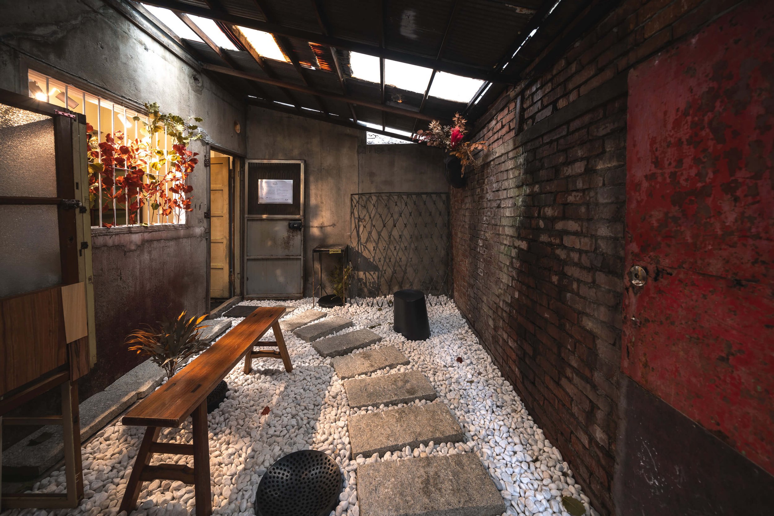 台中 Until 室內設計 Feng Cafe 奉咖啡老宅庭院，紅磚牆與白色碎石步道，木質長凳旁擺放植栽，屋頂透光天窗