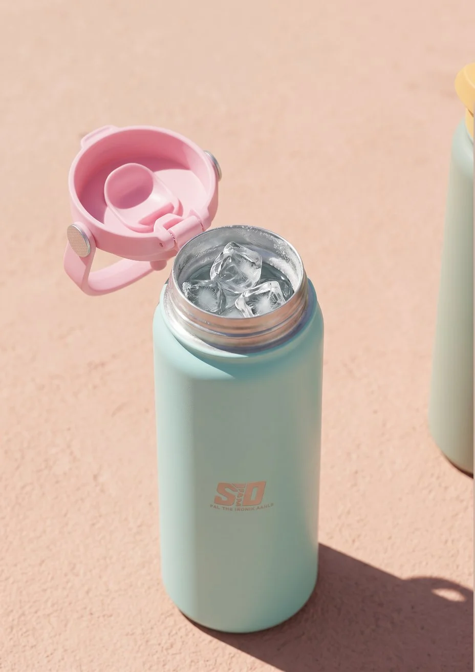 A light blue insulated water bottle with the lid open, filled with ice cubes, with a pink lid resting beside it on a pink surface.