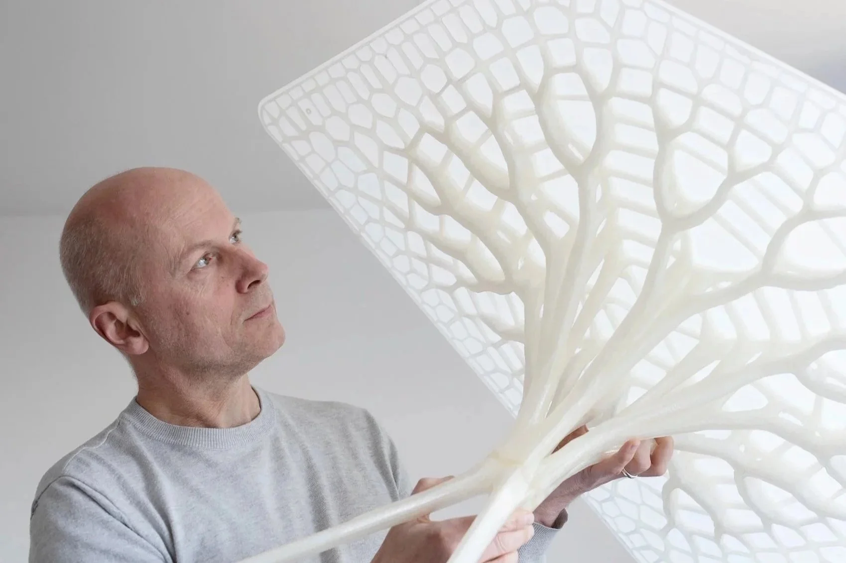 Michael Pawlyn holding a white, tree-shaped sculpture with intricate, web-like branches, looking at it with interest.
