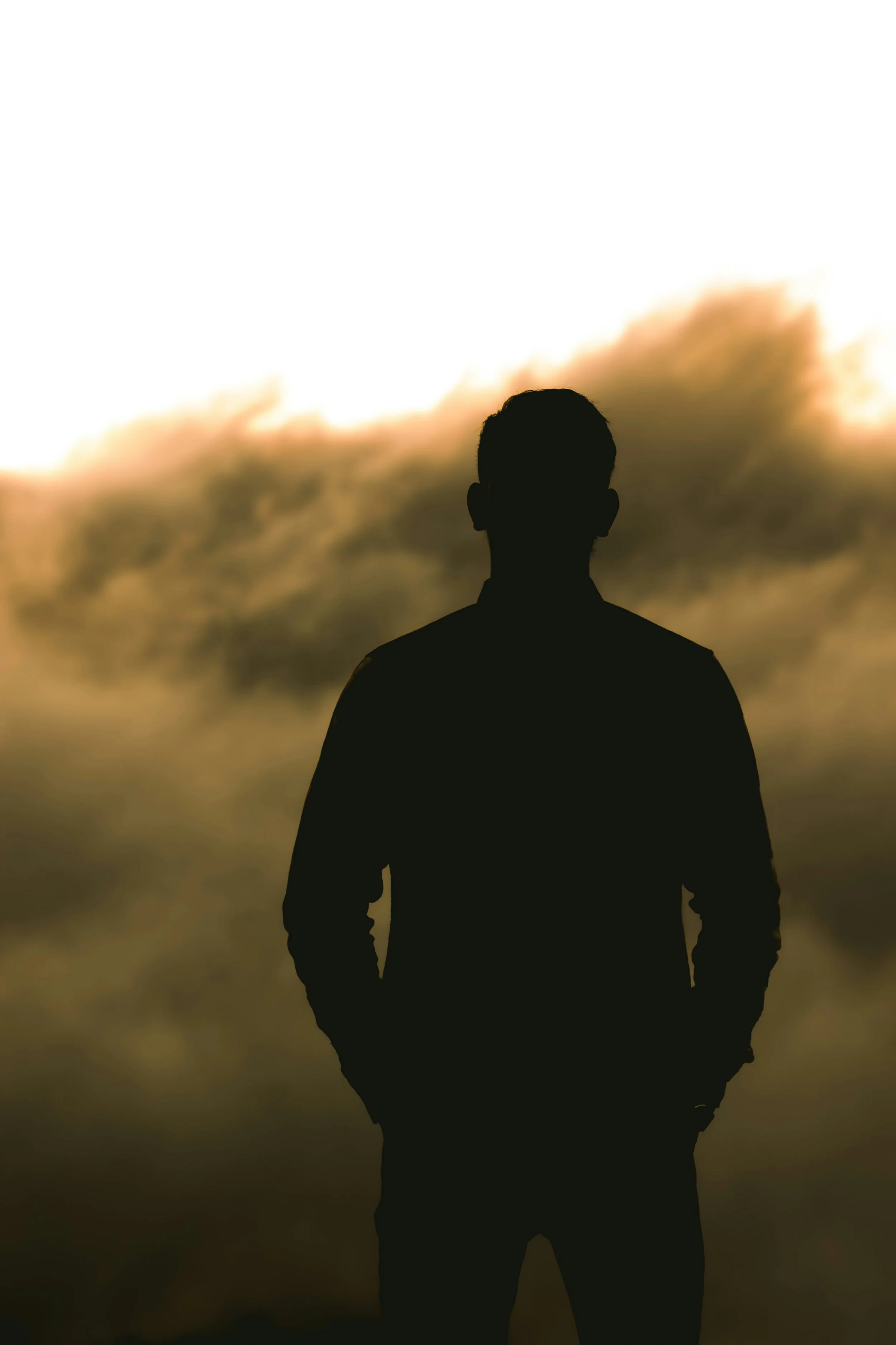 Silhouette of a person standing outdoors against a cloudy sky at sunset.