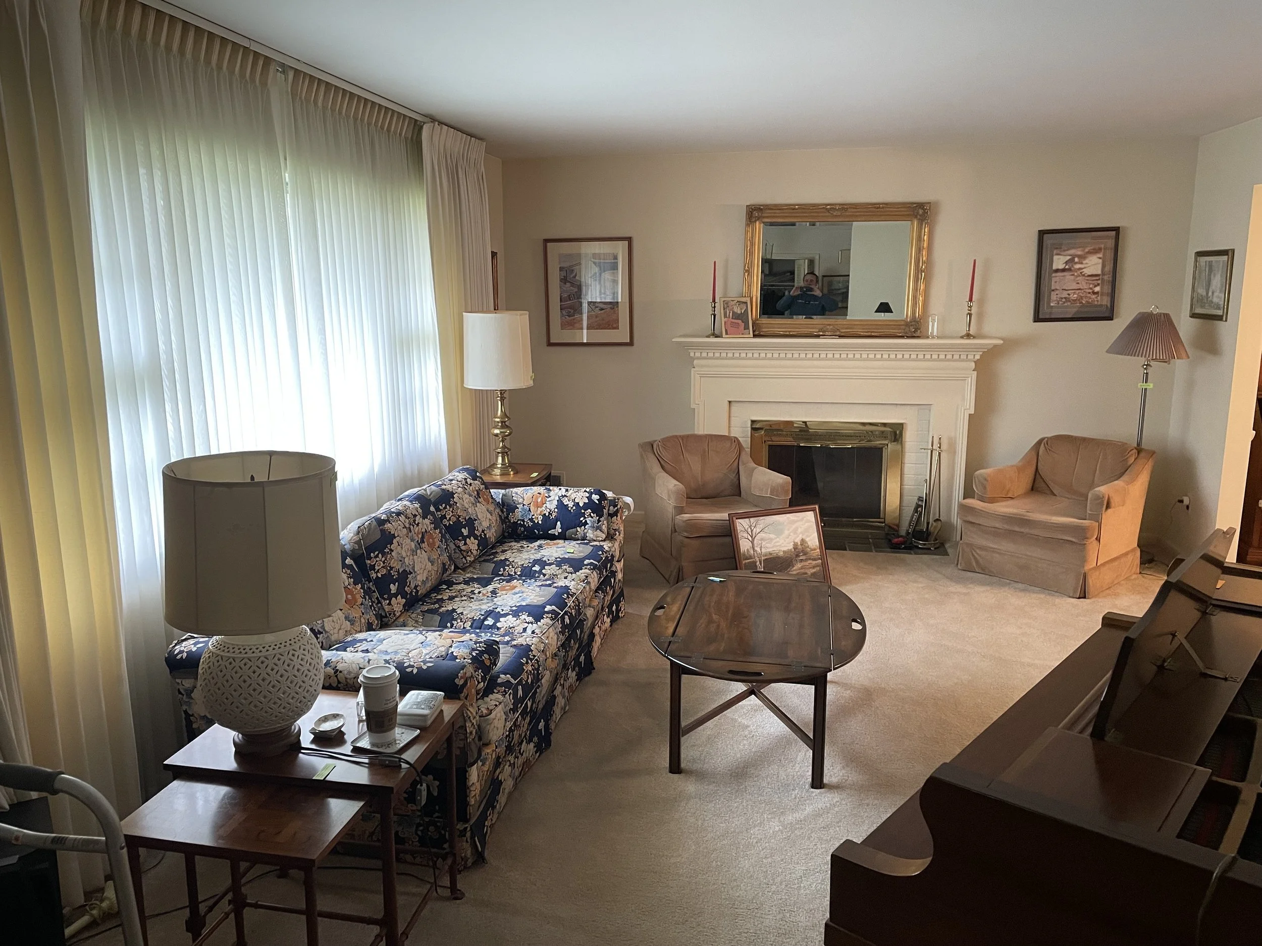 Traditional living room with a blue floral sofa, brick fireplace with gilded mirror, and beige armchairs — the space where a pivotal family conversation once took place.