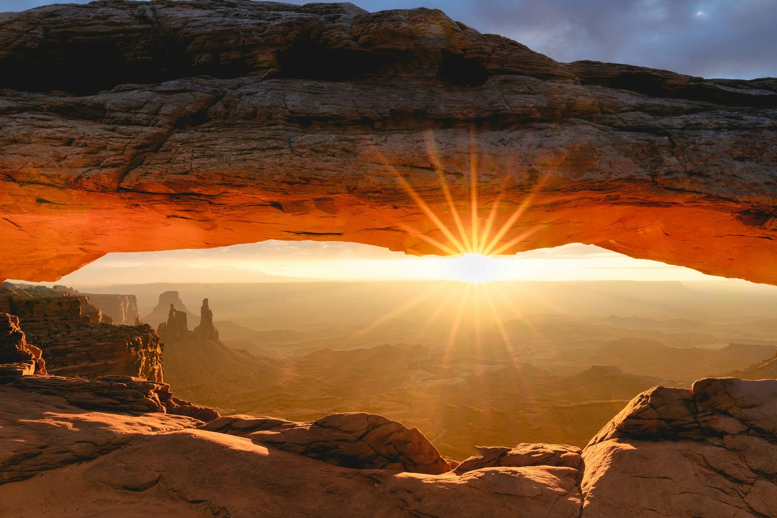 Sunrise shining through a desert rock arch, opening onto a wide canyon horizon — a visual metaphor for stepping out of the gilded cage into open sky.