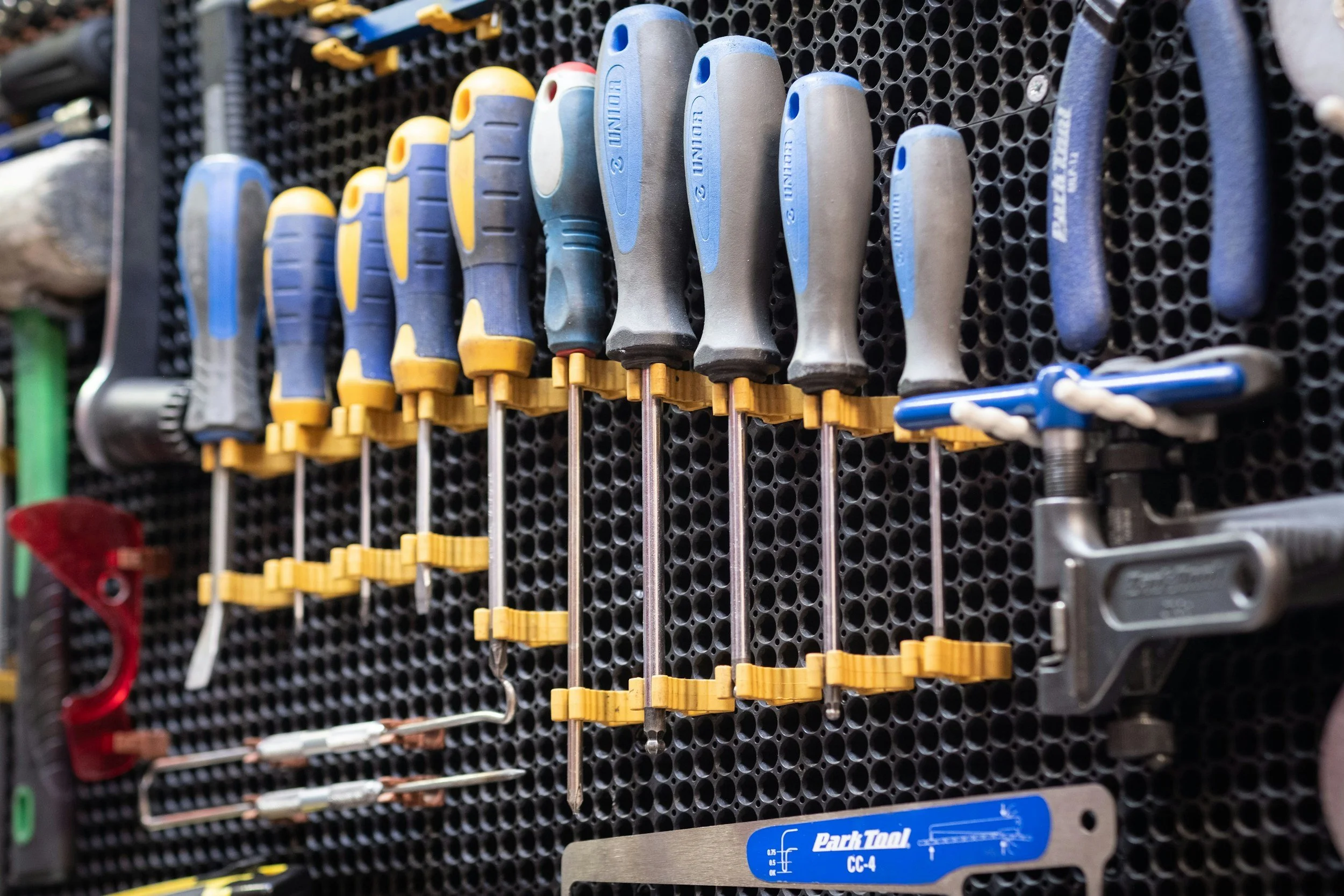 Row of yellow and blue screwdrivers organized by size on a black pegboard in a mechanic's workshop.