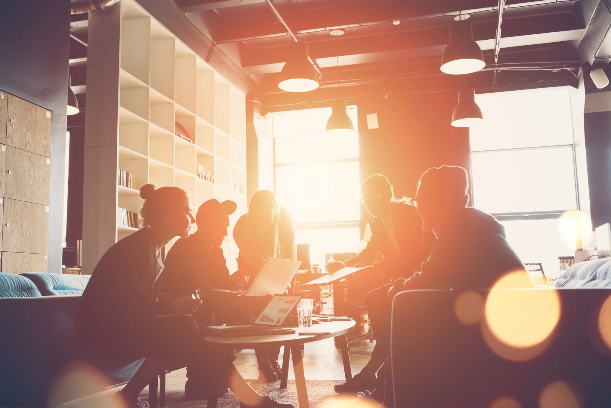 People silhouetted in warm golden light around a table in a casual coworking space representing purposeful Next Endeavor work
