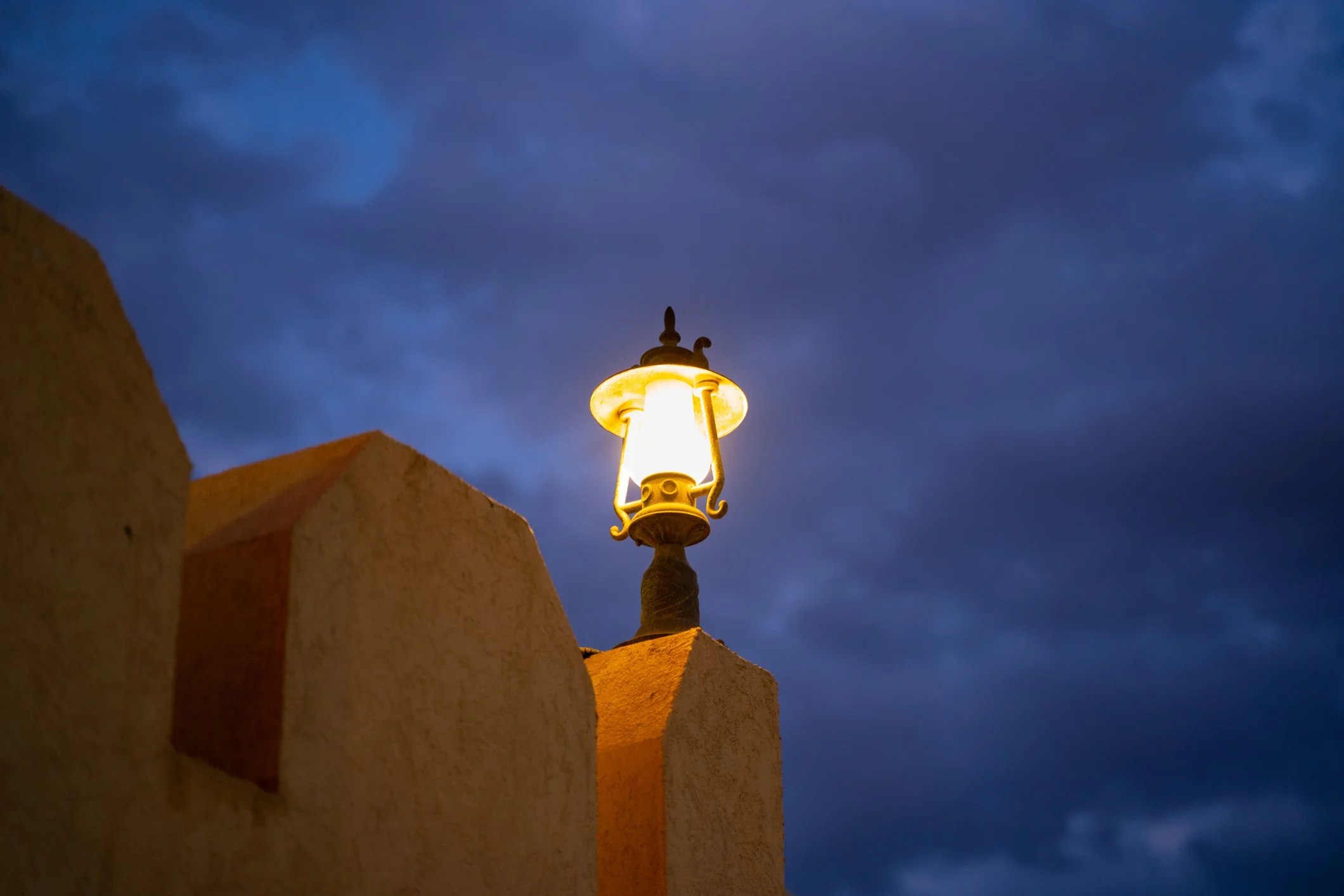 Glowing lantern on an adobe-style wall under a dark blue evening sky. The light is still on in the quiet hour when retirement worries get loud.