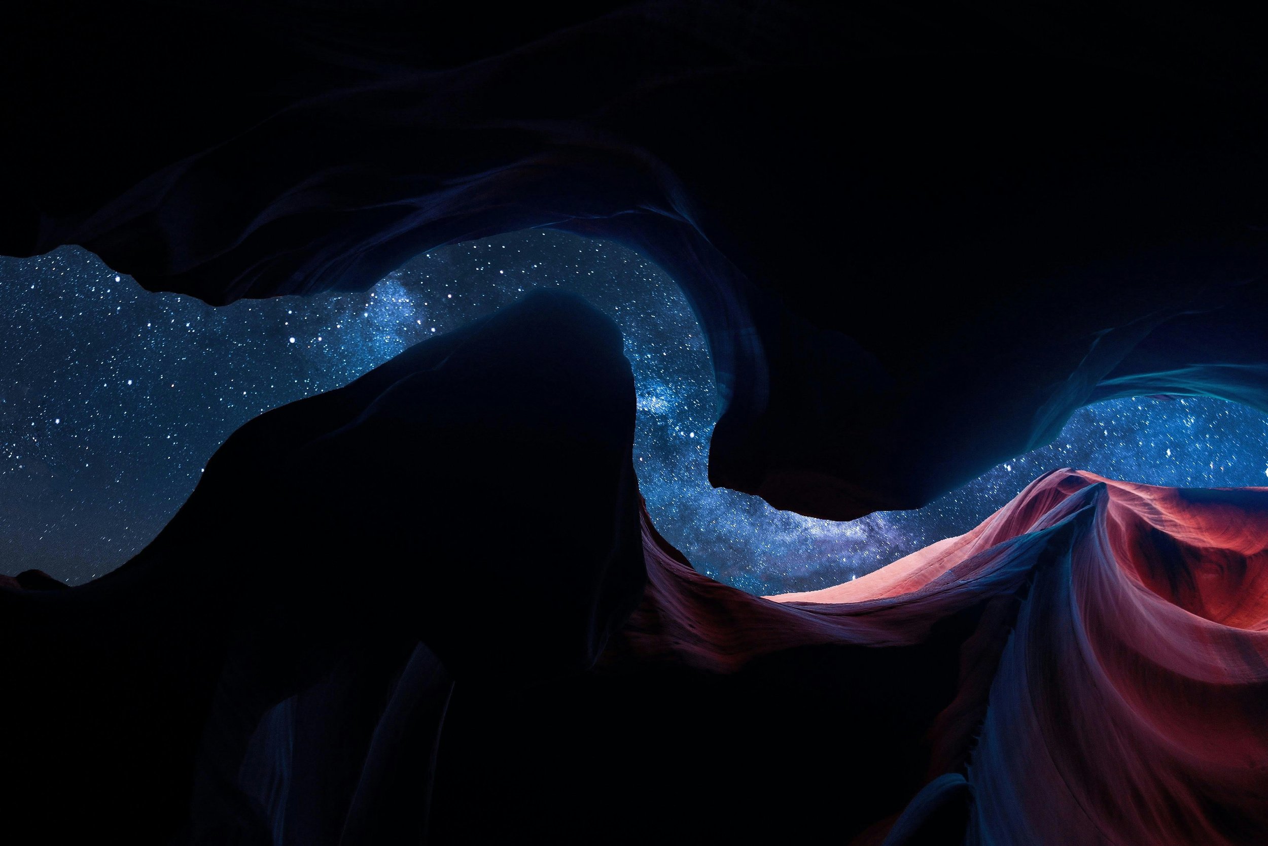 Dark rock formations with a view of a starry night sky and the Milky Way galaxy visible through a canyon or crevice.