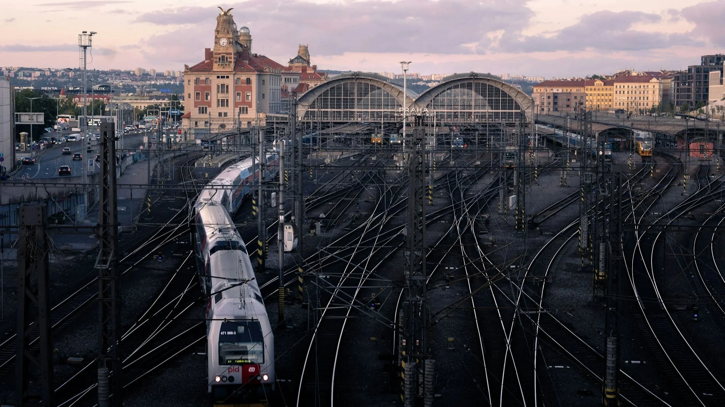 Wide view of Prague’s main train station at sunrise, with converging tracks and a train approaching the platforms.