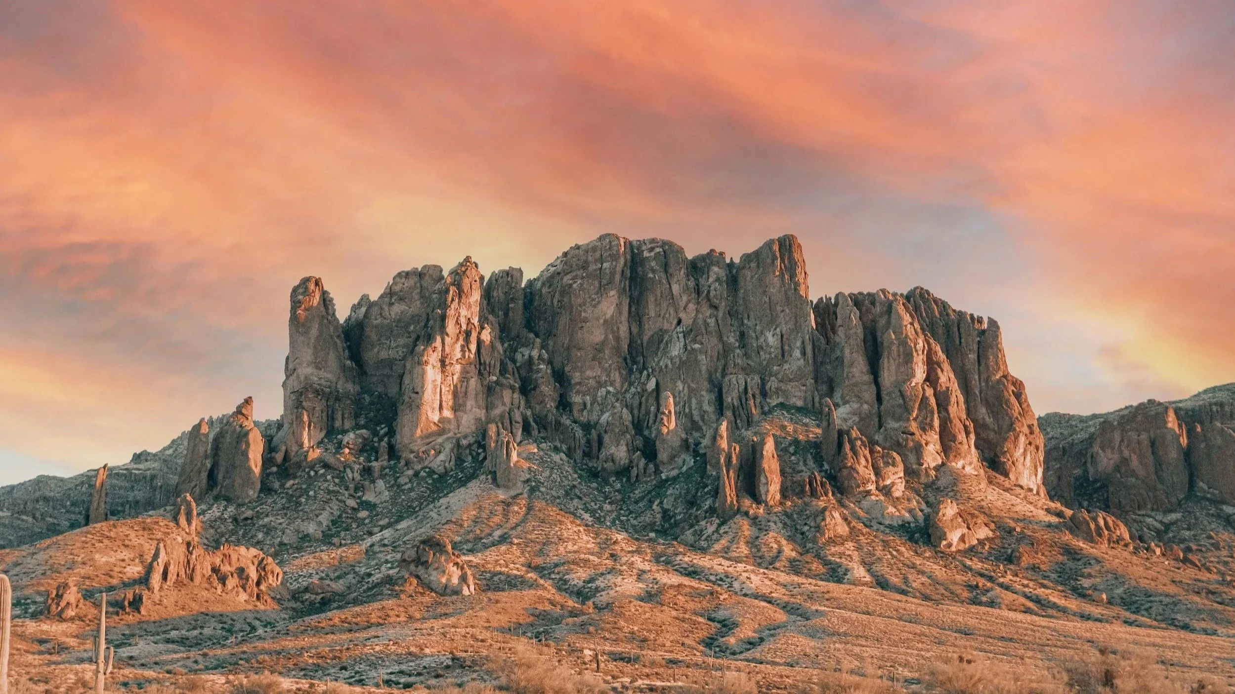 A dramatic Arizona desert mountain at sunrise with vivid pink and orange clouds — the landscape that shapes the Desert FI perspective.