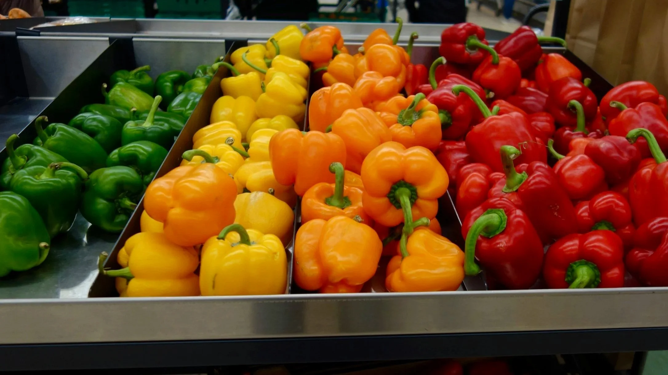 Grocery bins of green, yellow, orange and red bell peppers side by side.