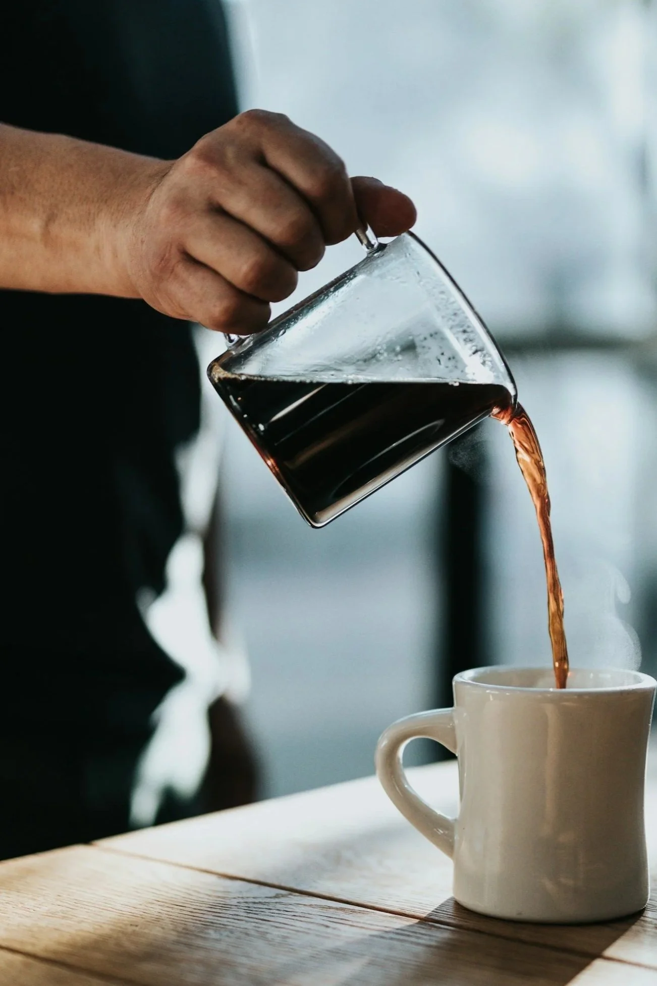 Close-up of hot coffee being poured into a ceramic mug on a wooden table, evoking morning rhythm and intentional daily routines.
