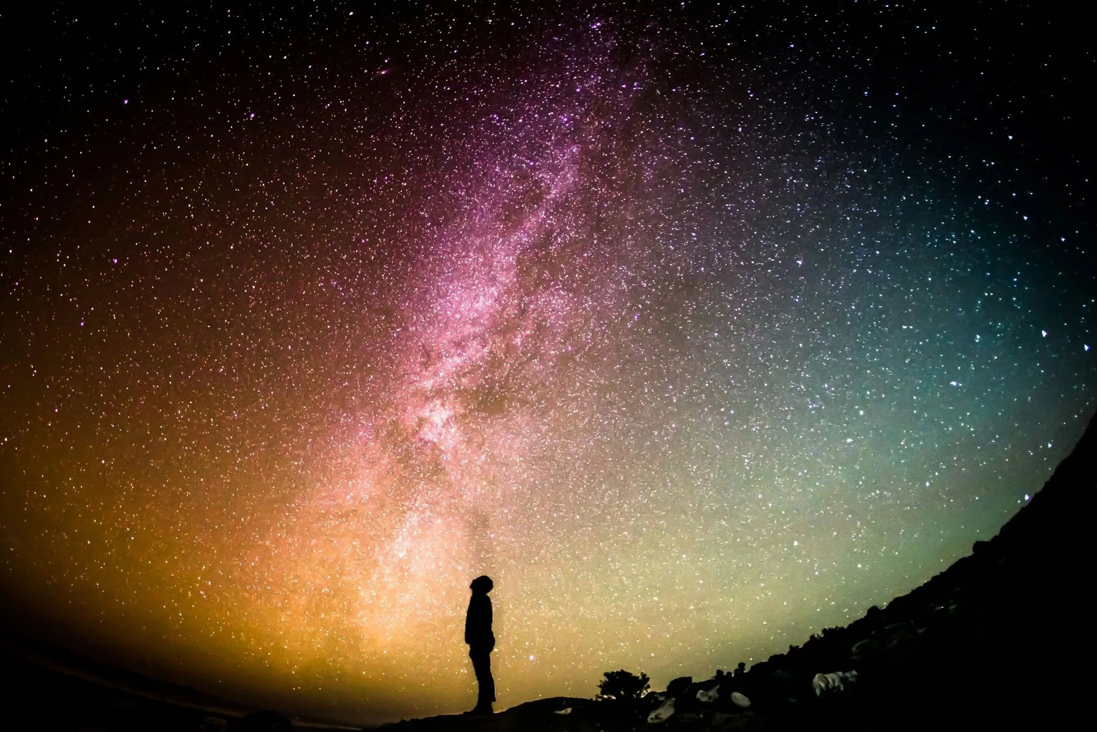 Silhouette standing beneath a vibrant Milky Way sky, looking upward in a moment of quiet reflection.