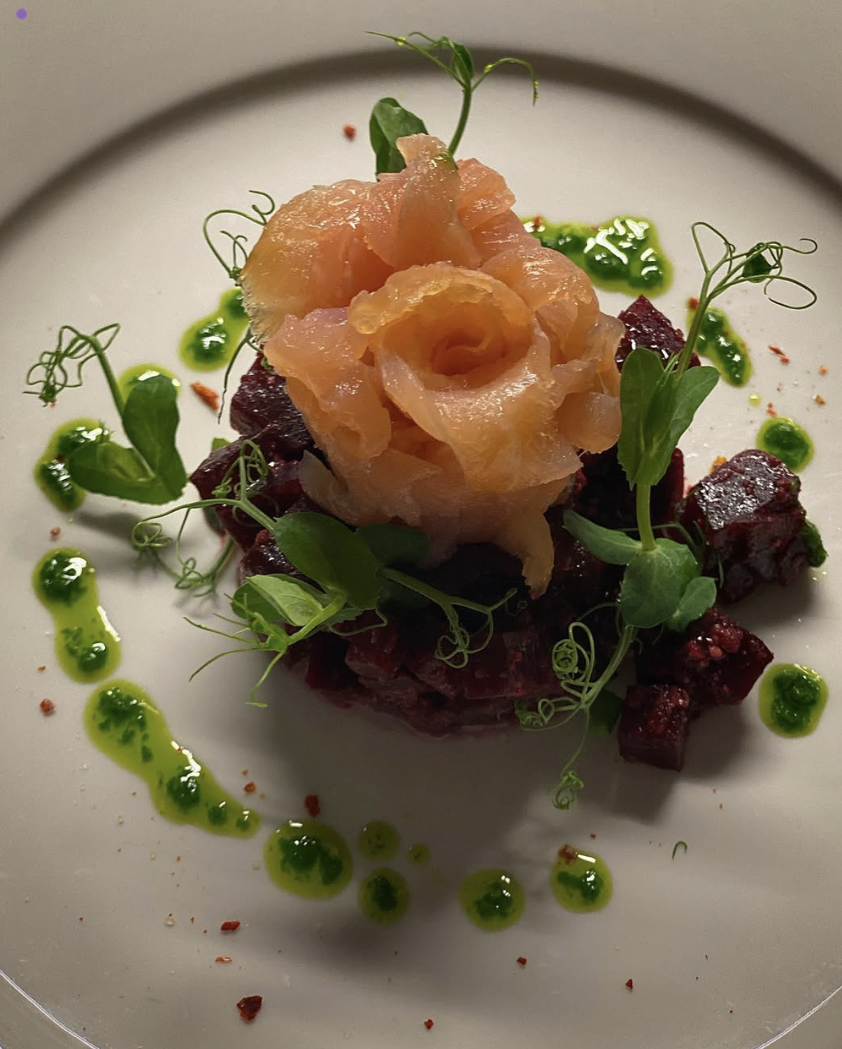 Gericht mit LAchs, Rote-Bete-Würfeln, grünen Saucen auf einem weißen Teller.