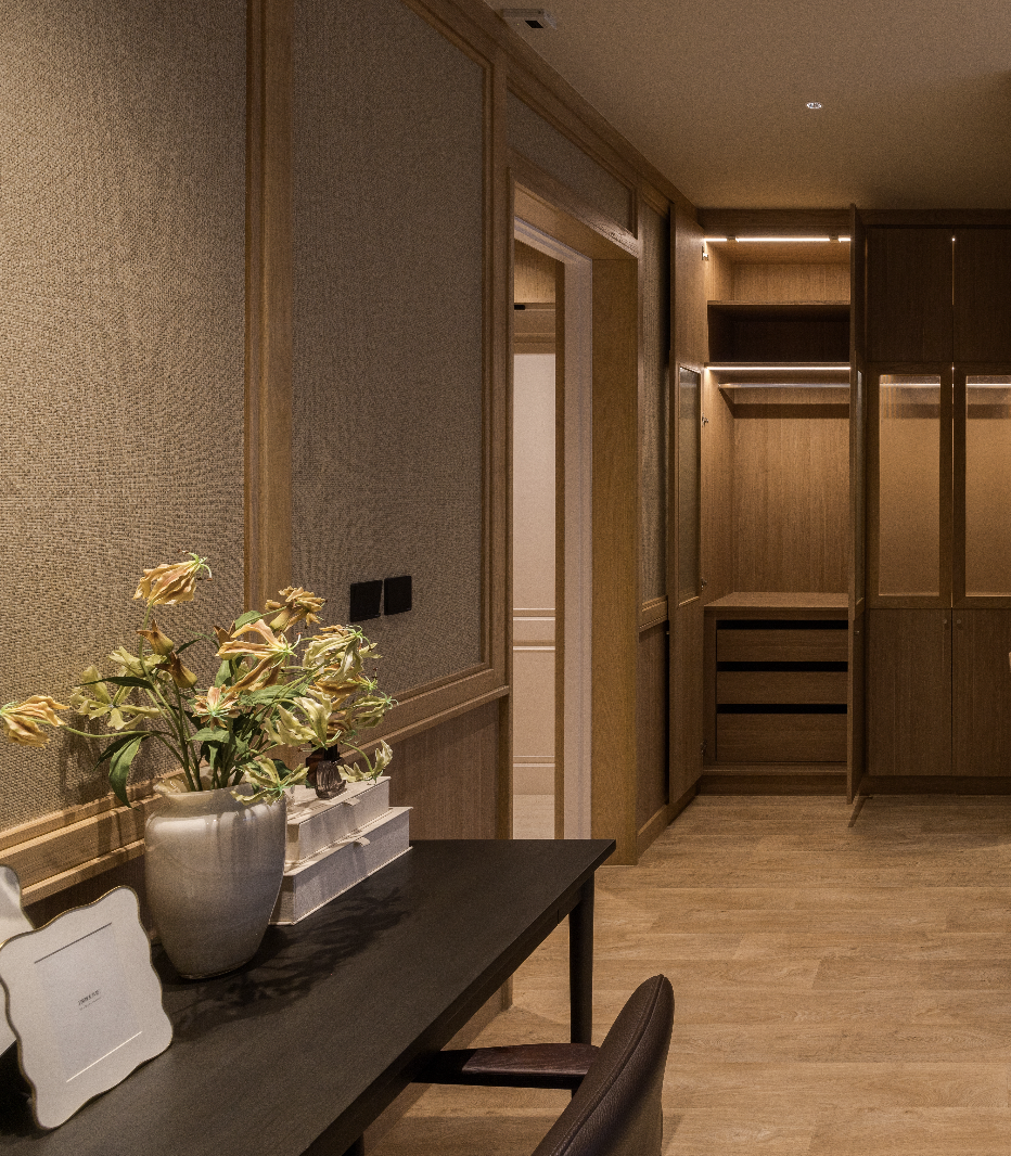 Interior view of a room with wooden wall panels, a black table with a flower vase, and a partially open closet with shelves and drawers.
