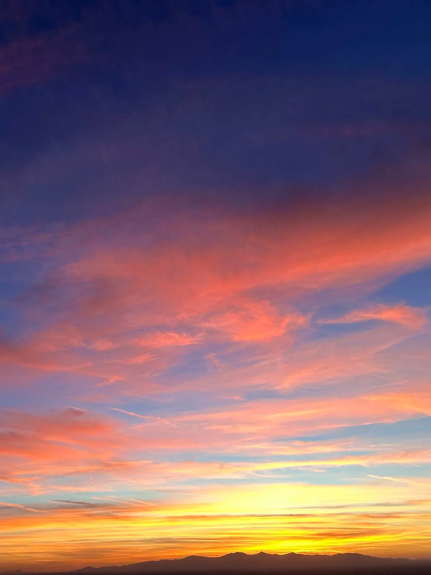 A colorful sunset sky with hues of pink, orange, yellow, and purple, with silhouettes of mountains at the horizon.