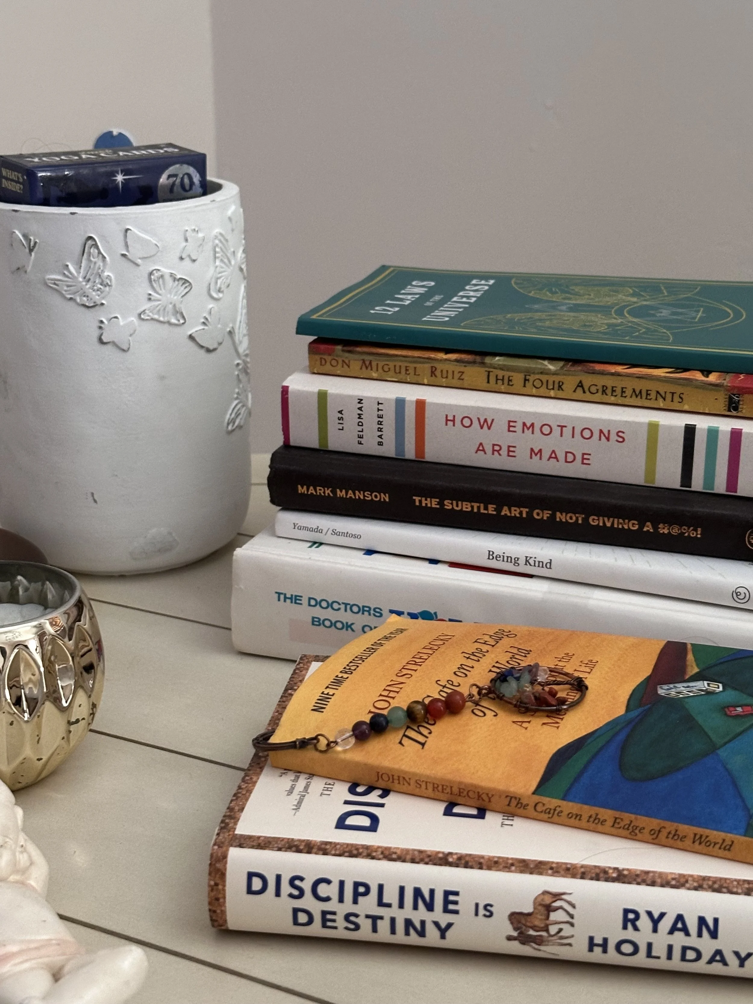 Stack of books on a white surface with a white decorative vase and a small metallic candle holder nearby.