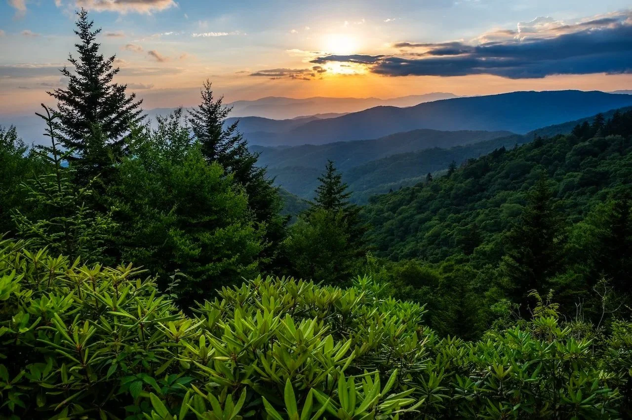 A scenic view of a lush green mountain range during sunset with layered mountains and a partly cloudy sky.