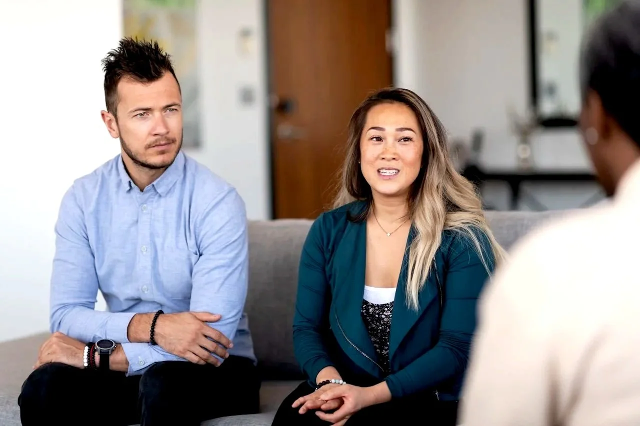 Three people in a meeting room having a discussion. Two are facing the camera, while the third person's back is visible.