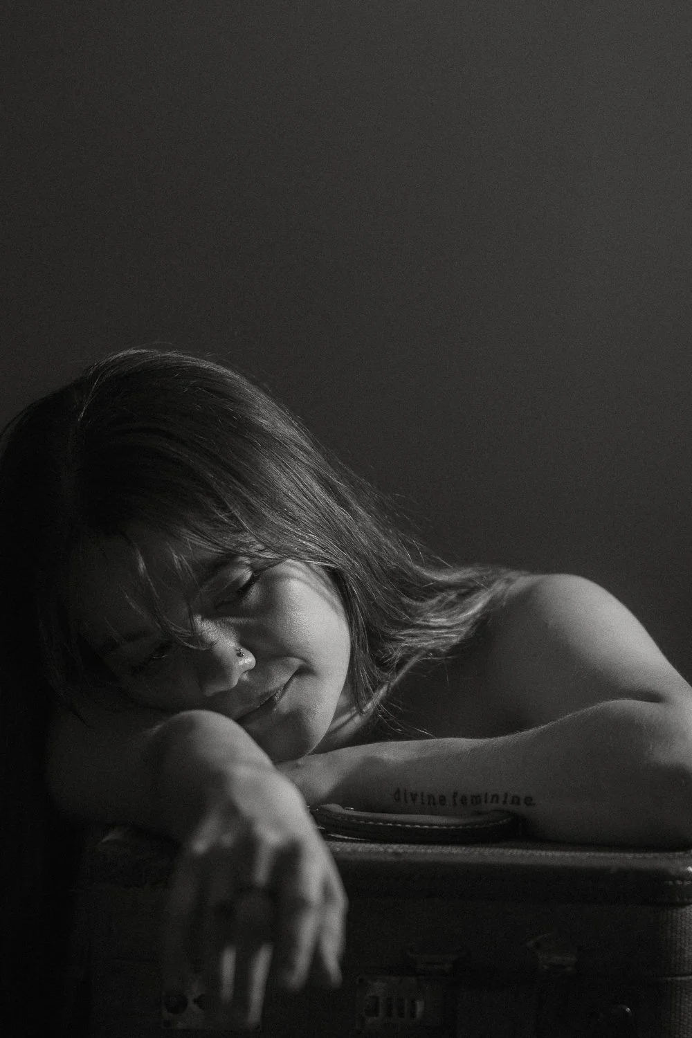 Black and white photo of a young woman with long hair resting her head on her arm, smiling gently with closed eyes.