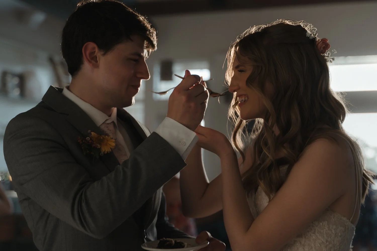 A man in a suit is feeding a woman in a wedding dress a piece of food with a fork at a wedding reception.